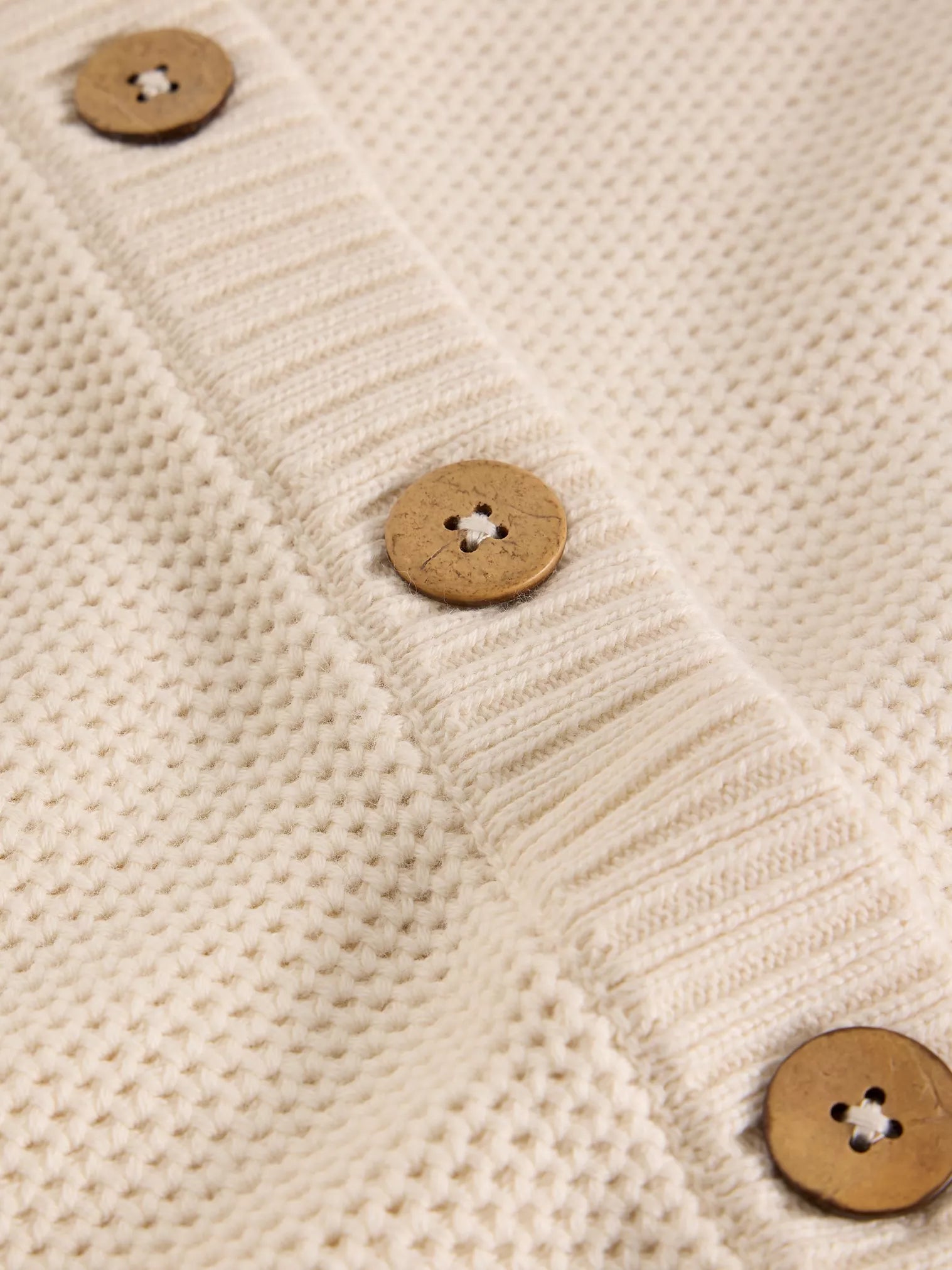 Close-up of a beige knitted fabric with wooden buttons