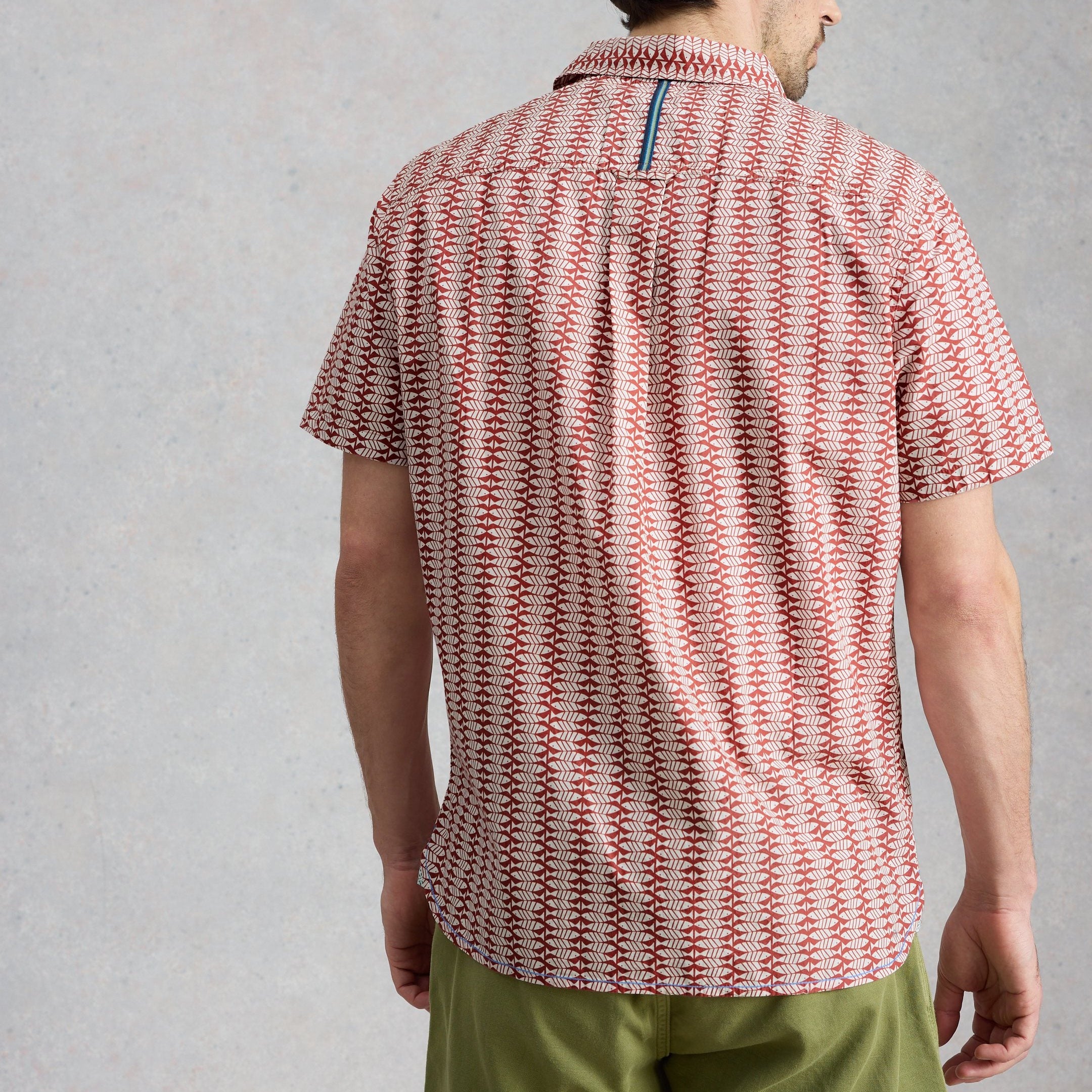 Person wearing a red and white patterned shirt with green pants on a gray background