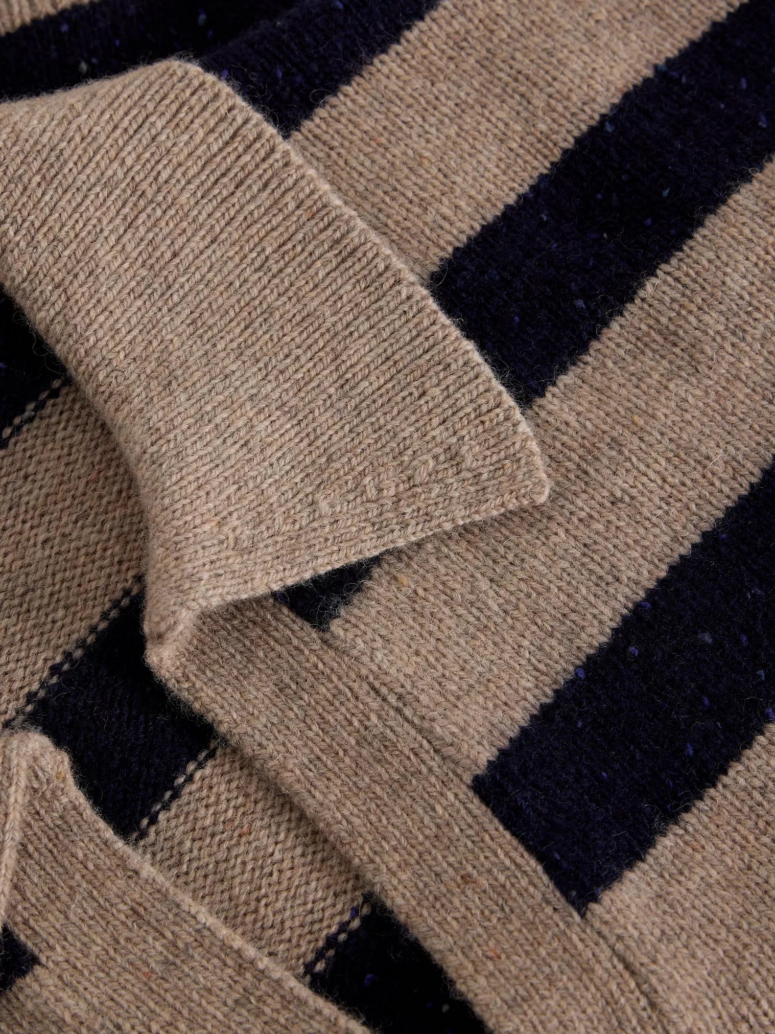 Close-up of a knit garment showing a beige collar and horizontal stripes in beige and very dark navy.