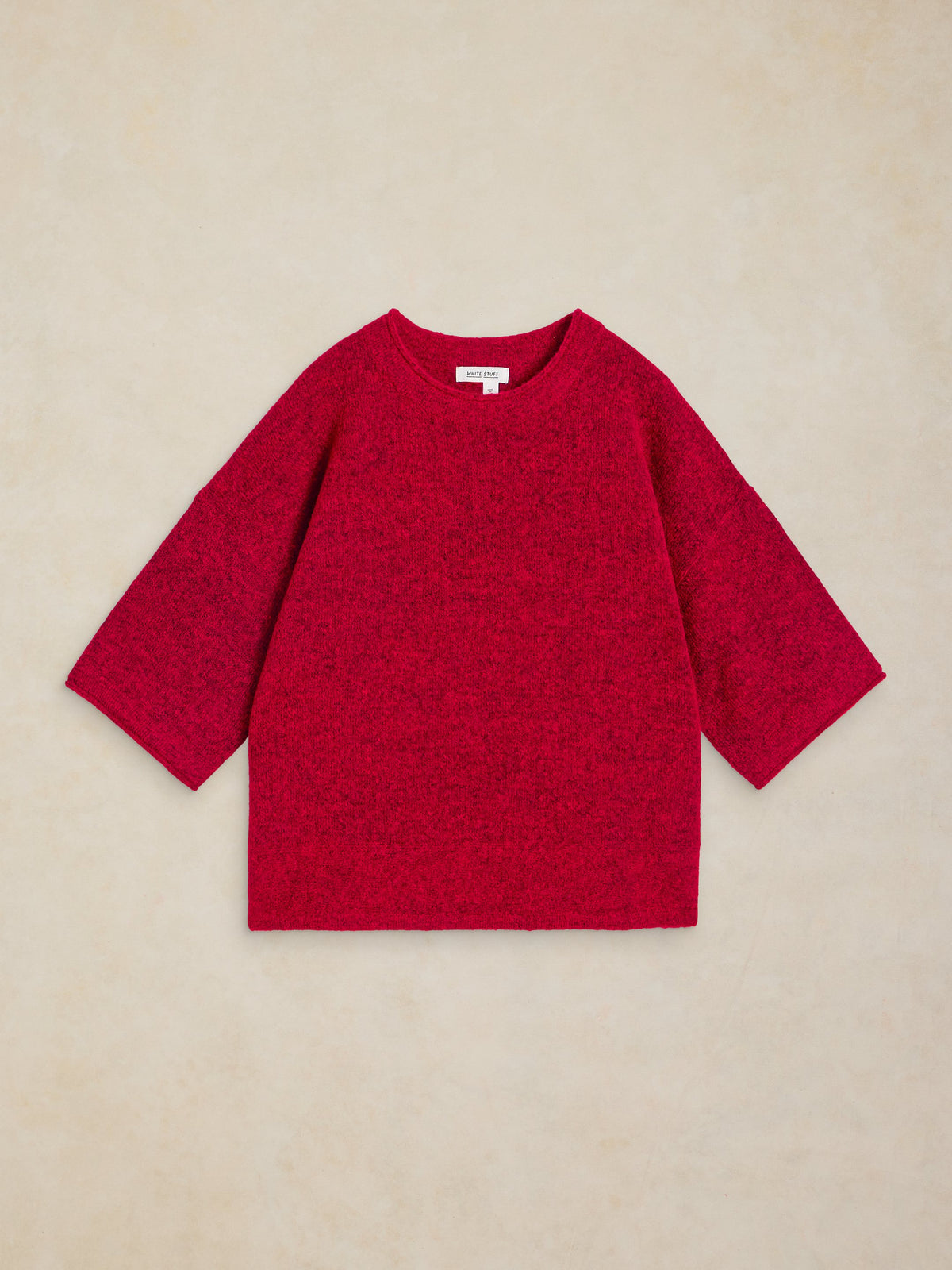 A bright red knit sweater with three-quarter sleeves, laid flat on a textured beige background.
