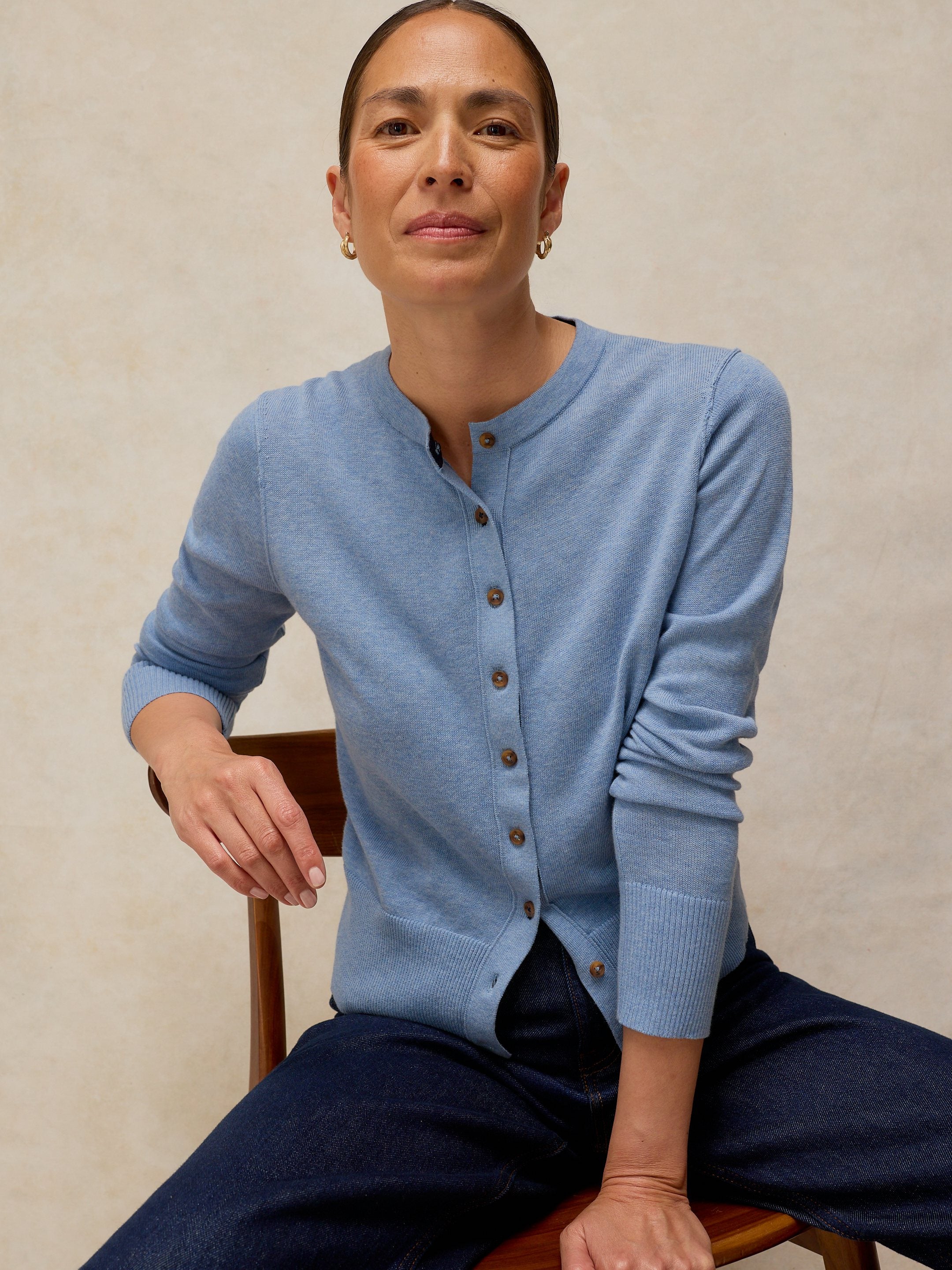 Woman wearing a light blue cardigan sitting on a chair against a beige background