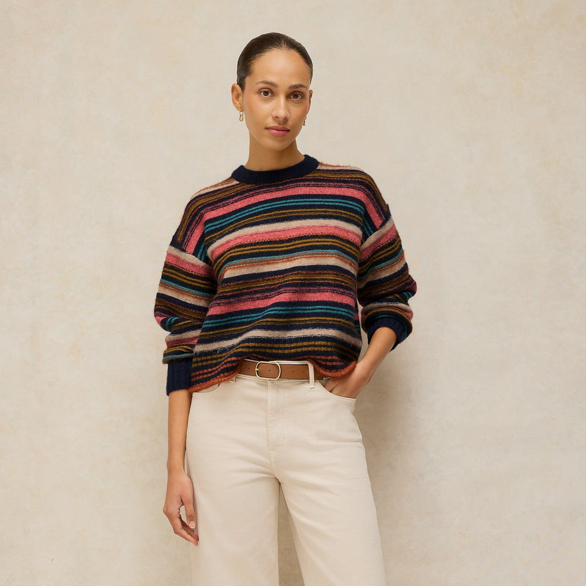Woman wearing a striped sweater and white pants against a plain background