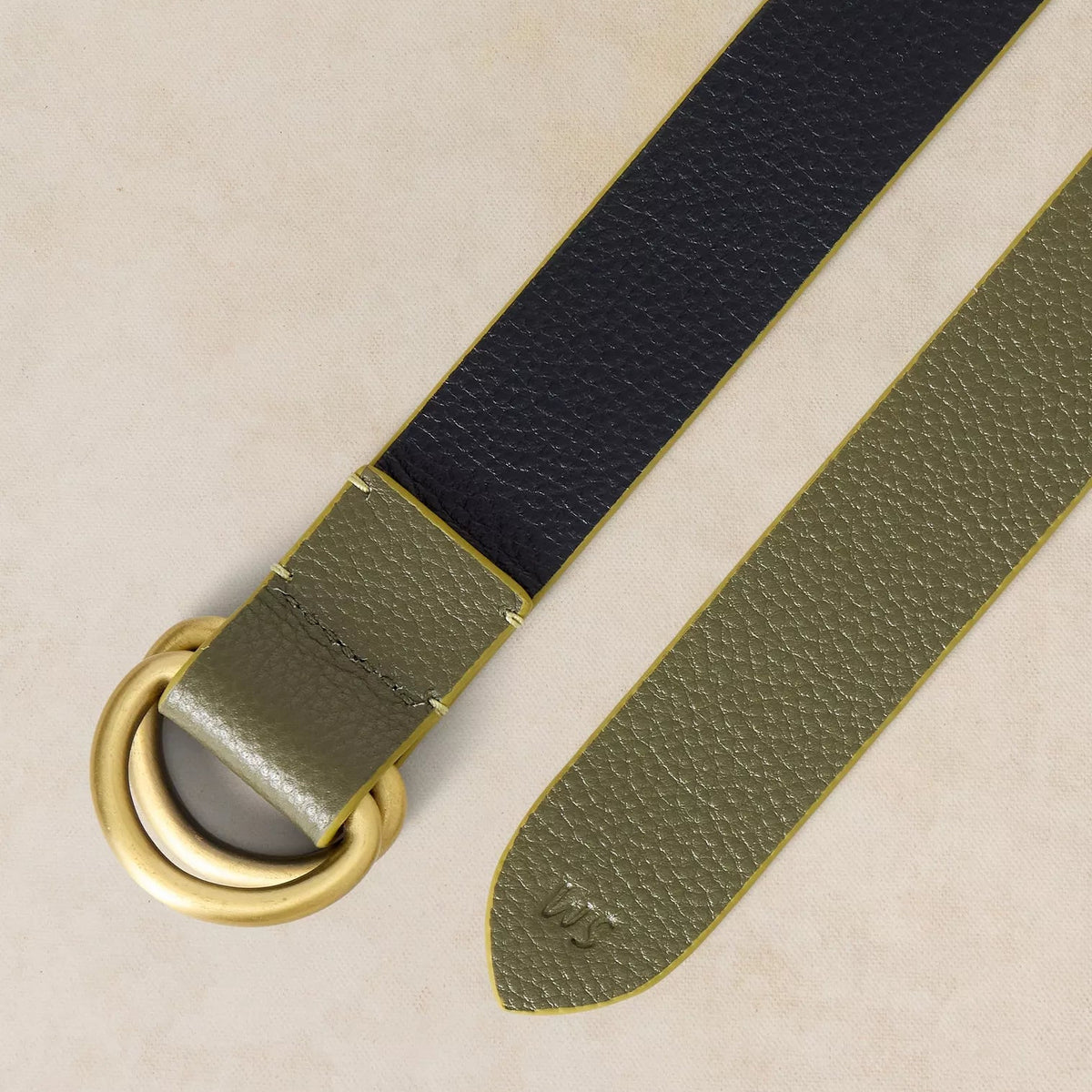 A close-up of a leather belt with a two-tone design, featuring a black upper section and an olive green lower section, finished with a gold-tone metal D-ring and tip.