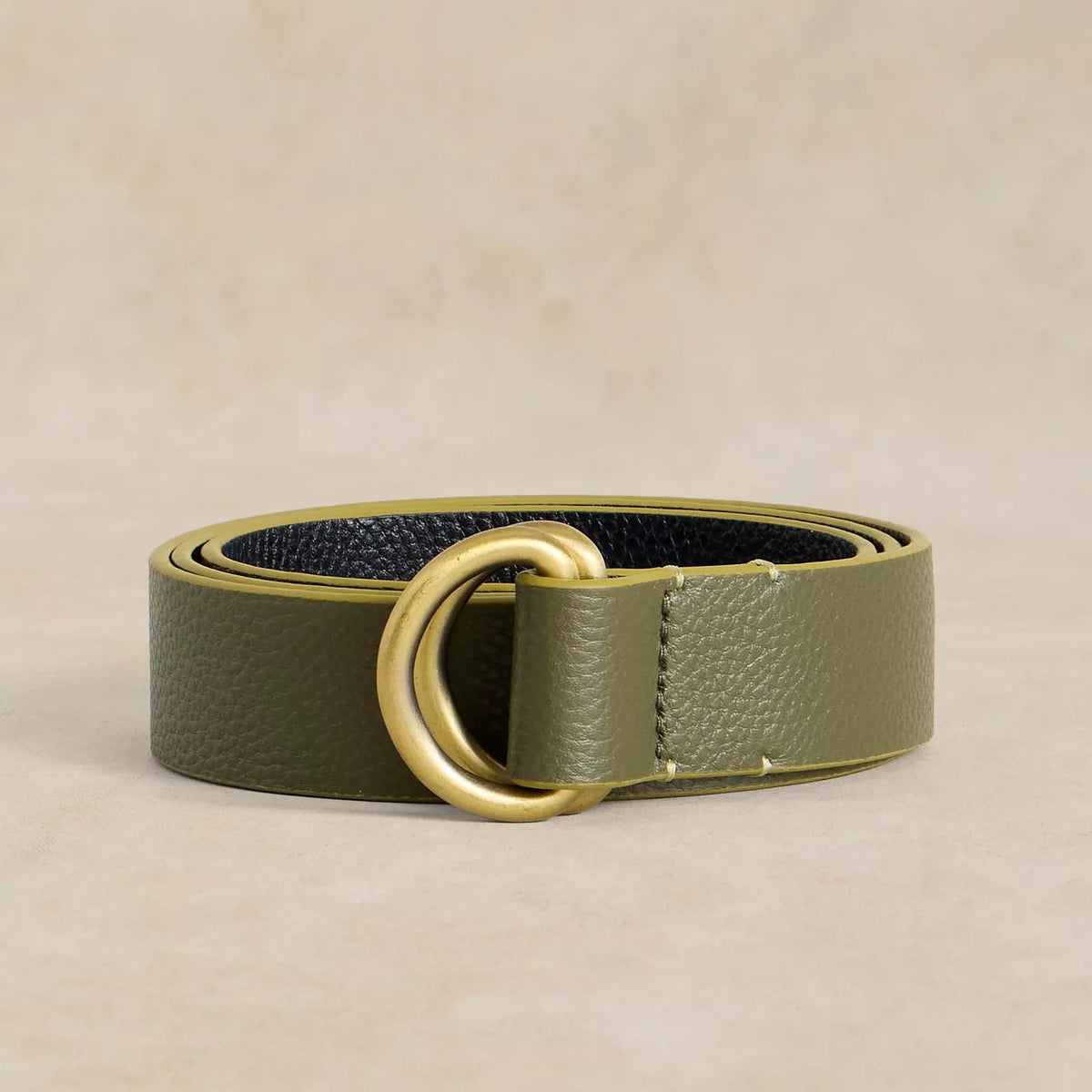 Green leather belt with a gold ring buckle on a beige background