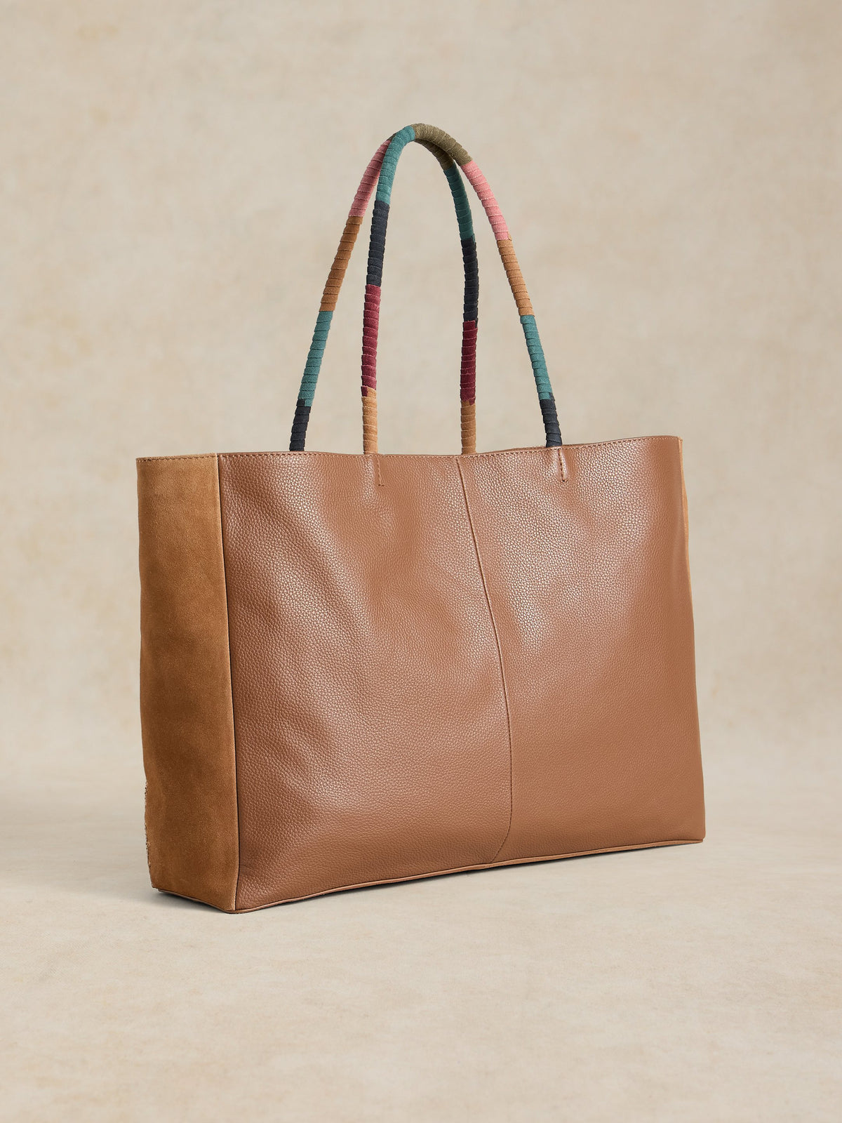 Brown leather tote bag with colorful handles on a beige background