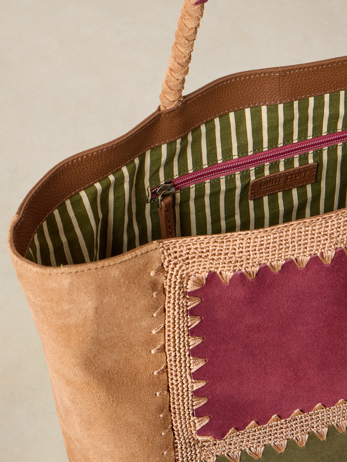 Close-up of a brown tote bag with striped lining and purple patchwork detail.