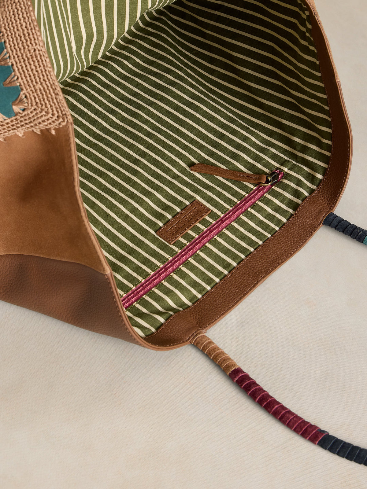 Close-up of a backpack with brown leather and striped fabric interior on a beige background