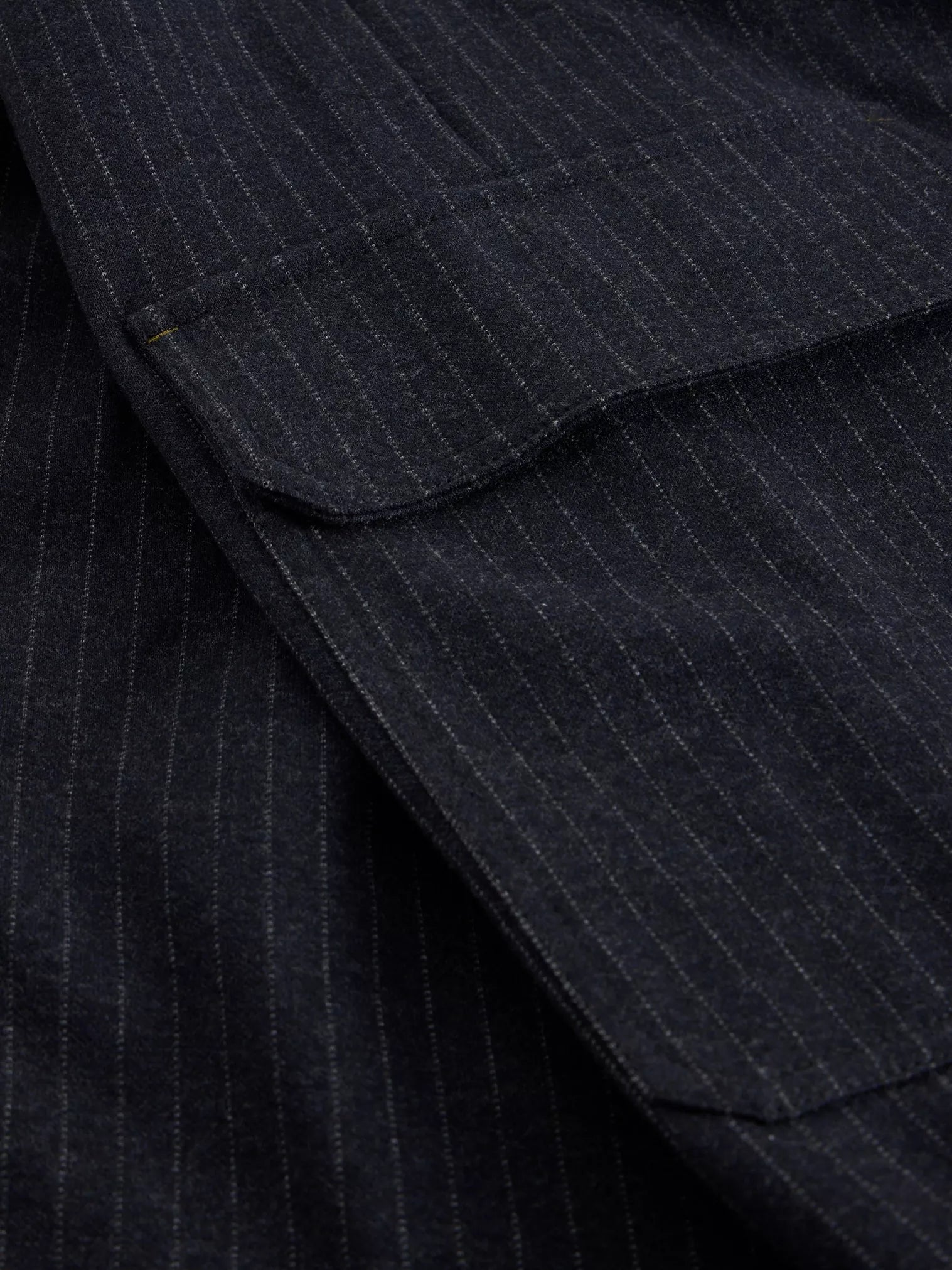 Close-up of dark navy blue fabric with fine vertical white pinstripes and a folded pocket detail.