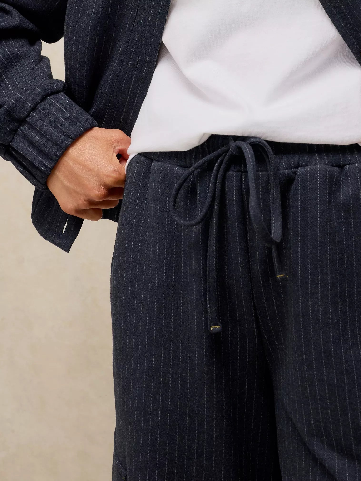 Close-up of a person wearing dark navy pinstriped trousers with a drawstring waist, styled with a white shirt and a matching dark cardigan.