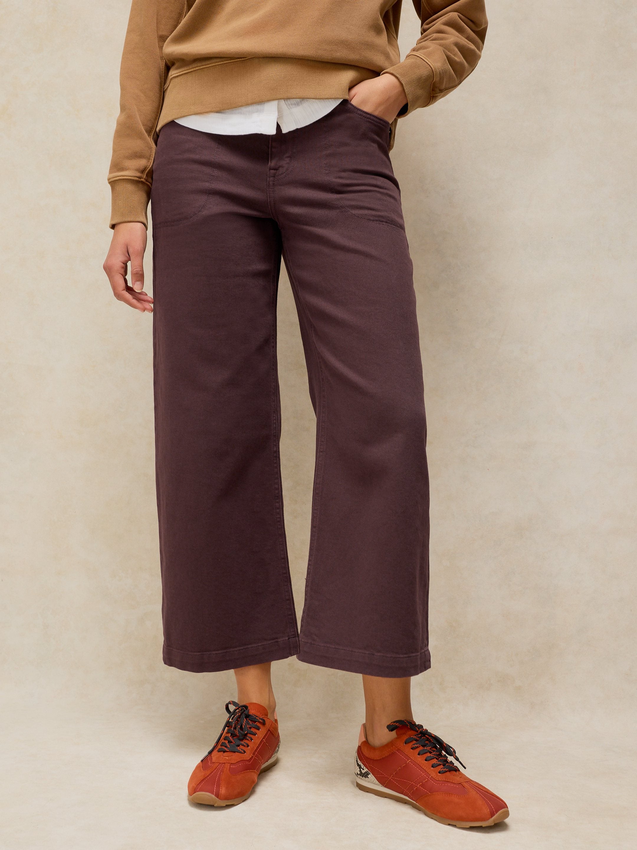 Person wearing brown sweater, white shirt, purple pants, and orange shoes on a beige background