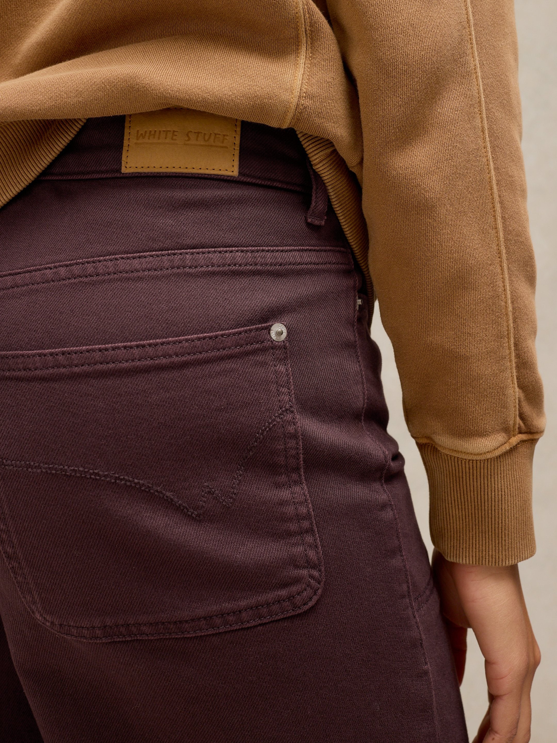 Person wearing a brown jacket and purple pants on a neutral background