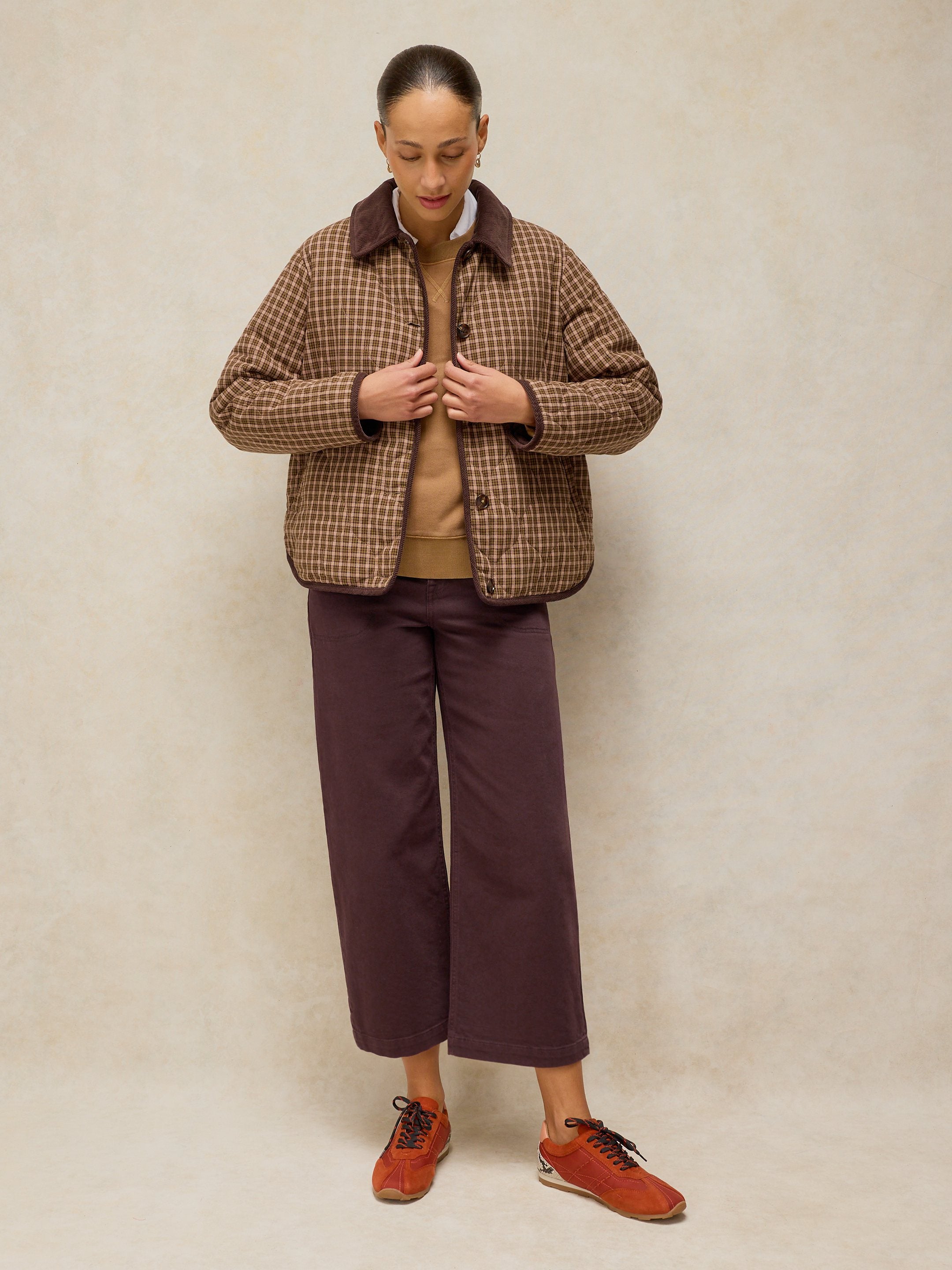 Person wearing a plaid jacket, brown shirt, purple pants, and orange shoes against a beige background