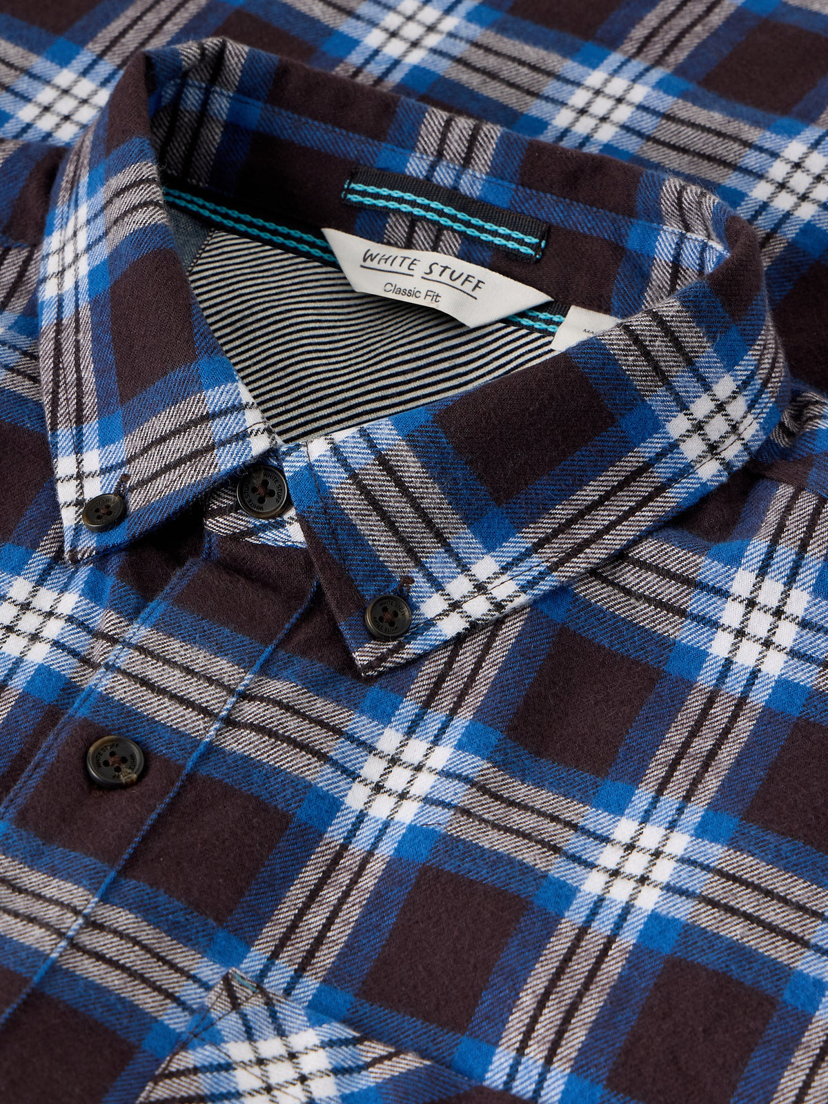 Close-up of a plaid button-down shirt by White Stuff, featuring a dark brown, blue, white, and black tartan pattern with a striped inner collar.