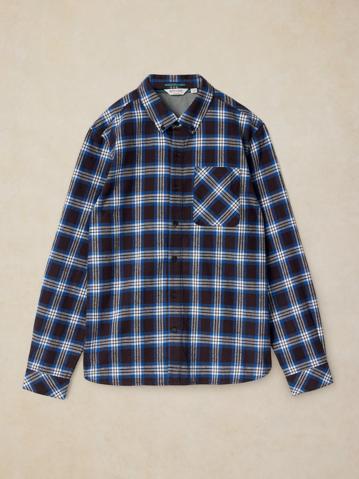 A long-sleeve button-up plaid shirt in navy blue, white, and light blue, laid flat against a textured beige background.
