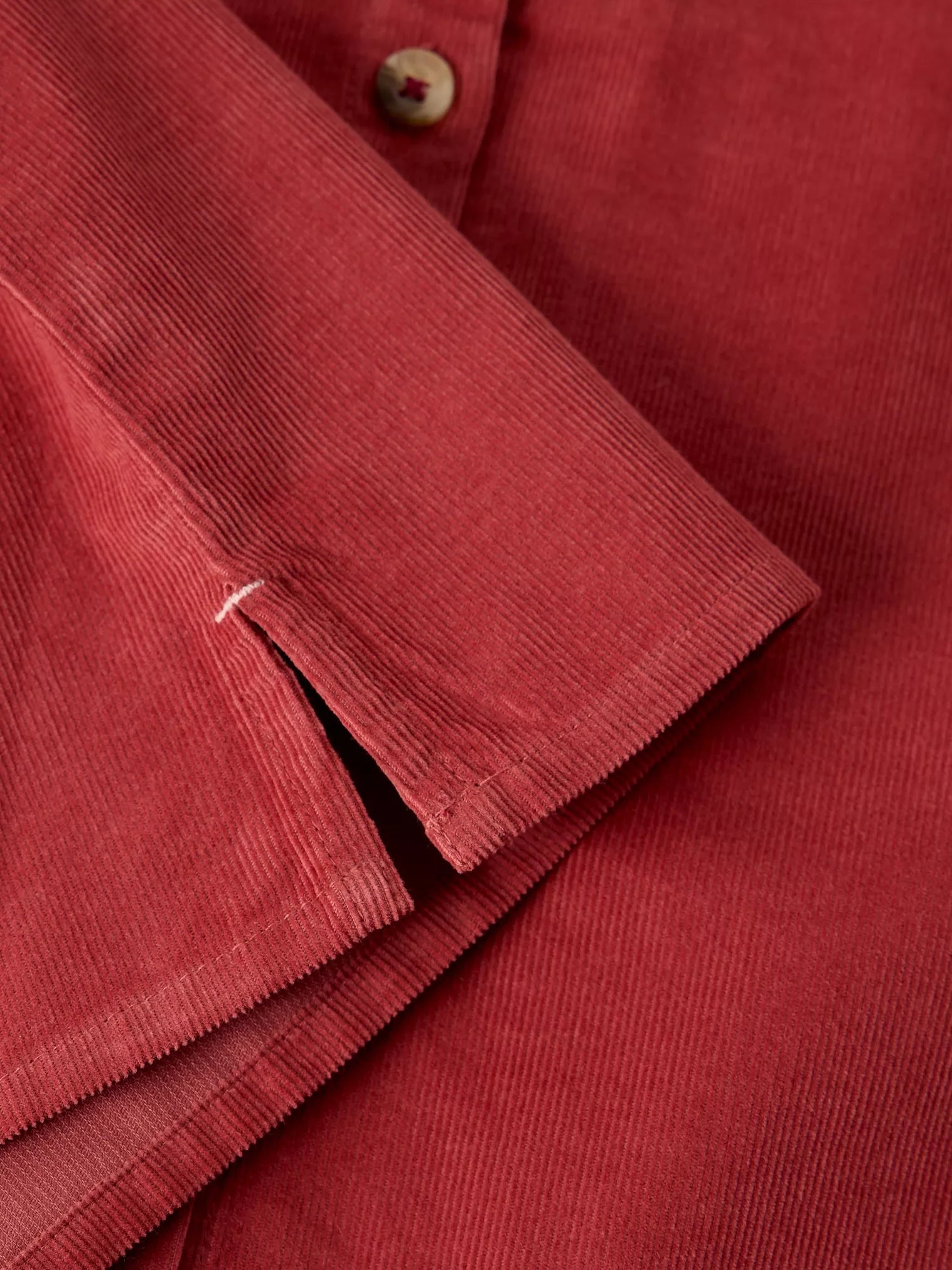 Close-up of a red corduroy shirt showing the textured fabric, button, and folded cuff detail.