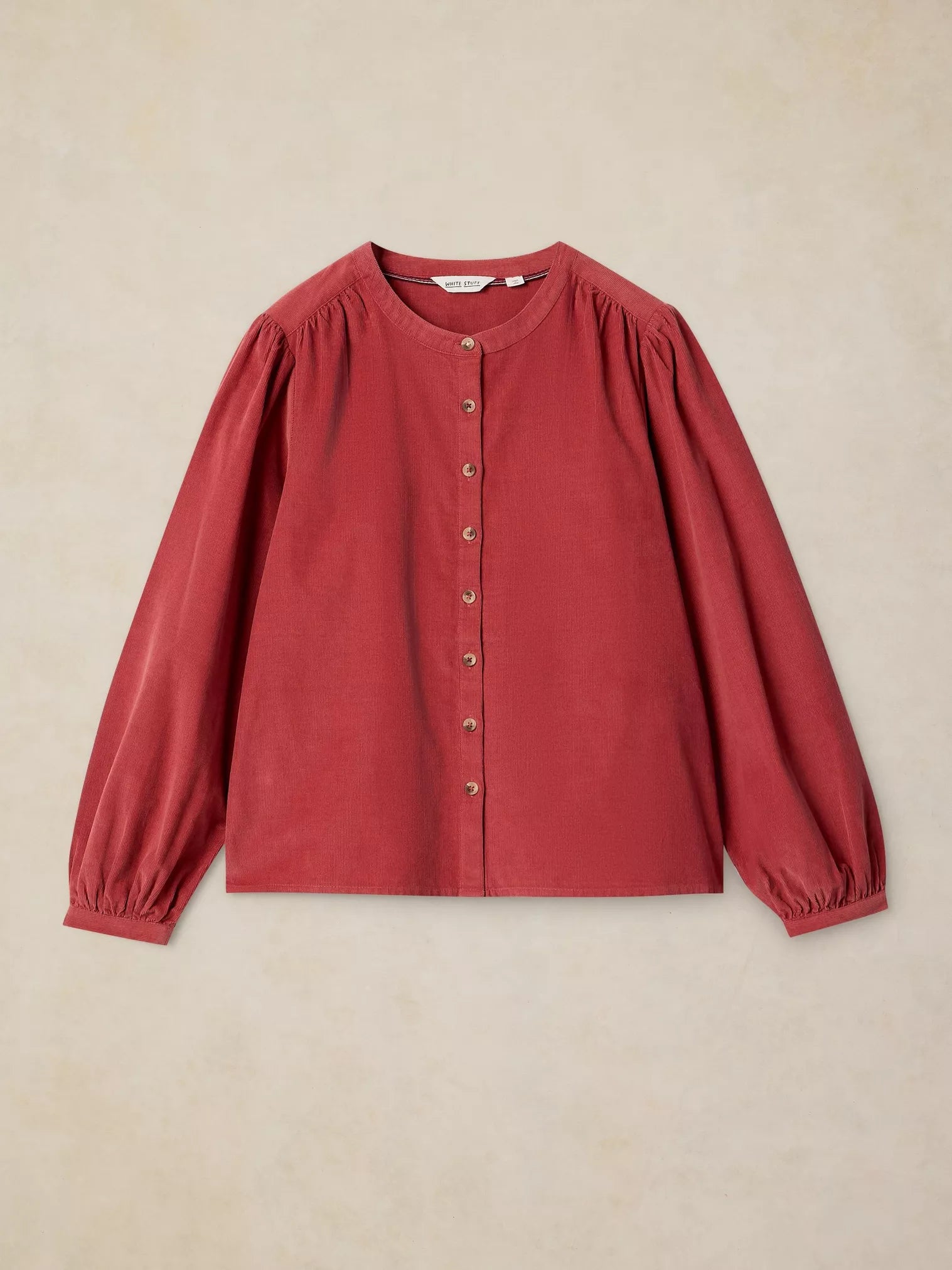 A dusty red long-sleeve blouse with gathered puff sleeves and a button-up front, laid flat against a textured beige background.