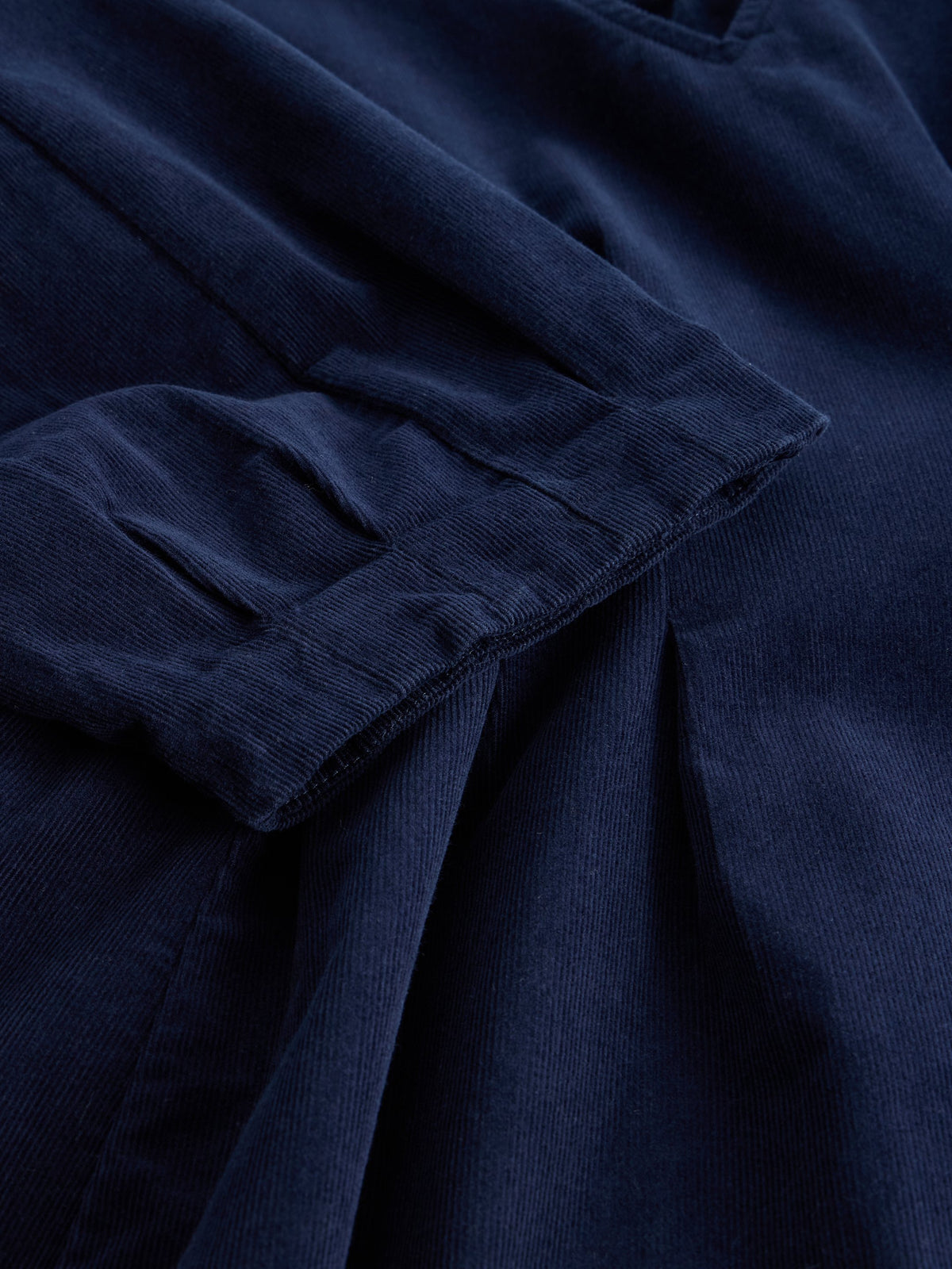 Close-up of a dark navy blue corduroy fabric with visible ribbed texture and folded pleats.