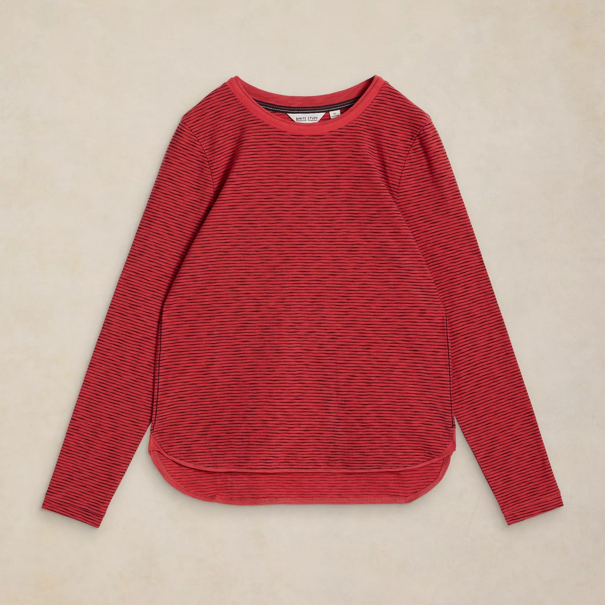 A red long-sleeve knit top with fine horizontal black stripes, laid flat on a textured beige background.