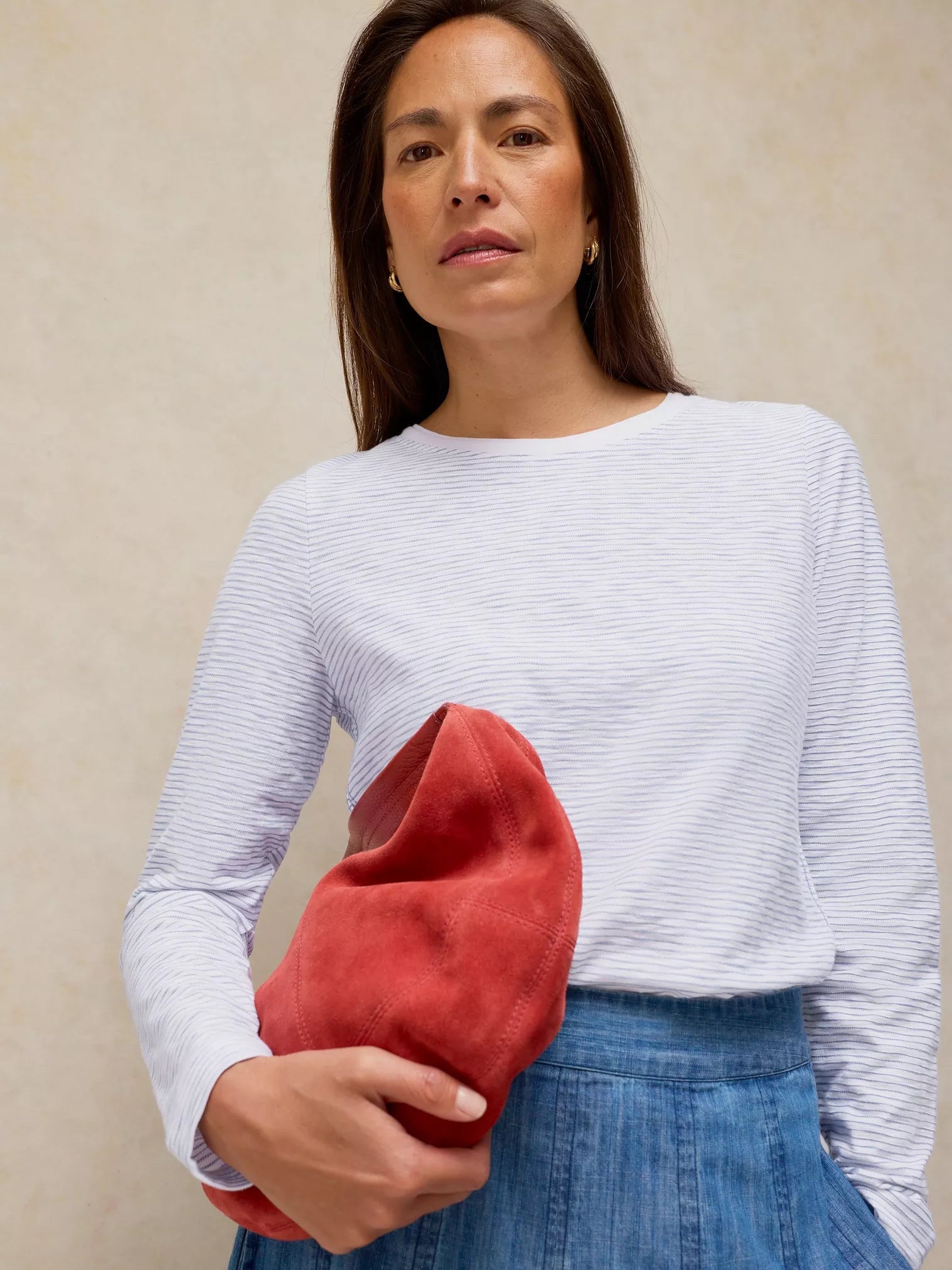 Woman holding a red suede clutch against a beige background