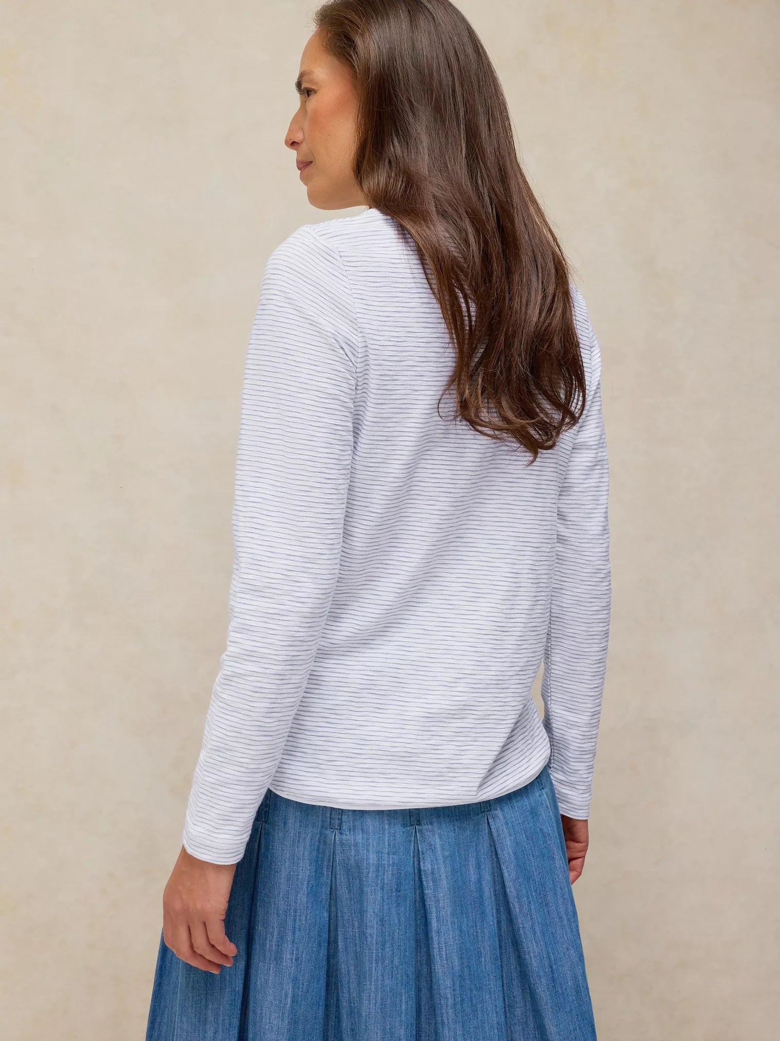 Woman wearing a light gray striped sweater and blue skirt against a beige background