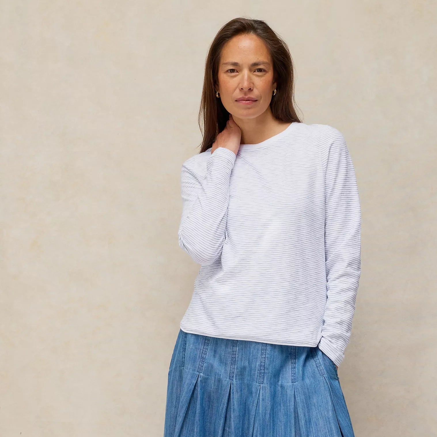 Woman wearing a light gray sweater and blue denim skirt against a beige background