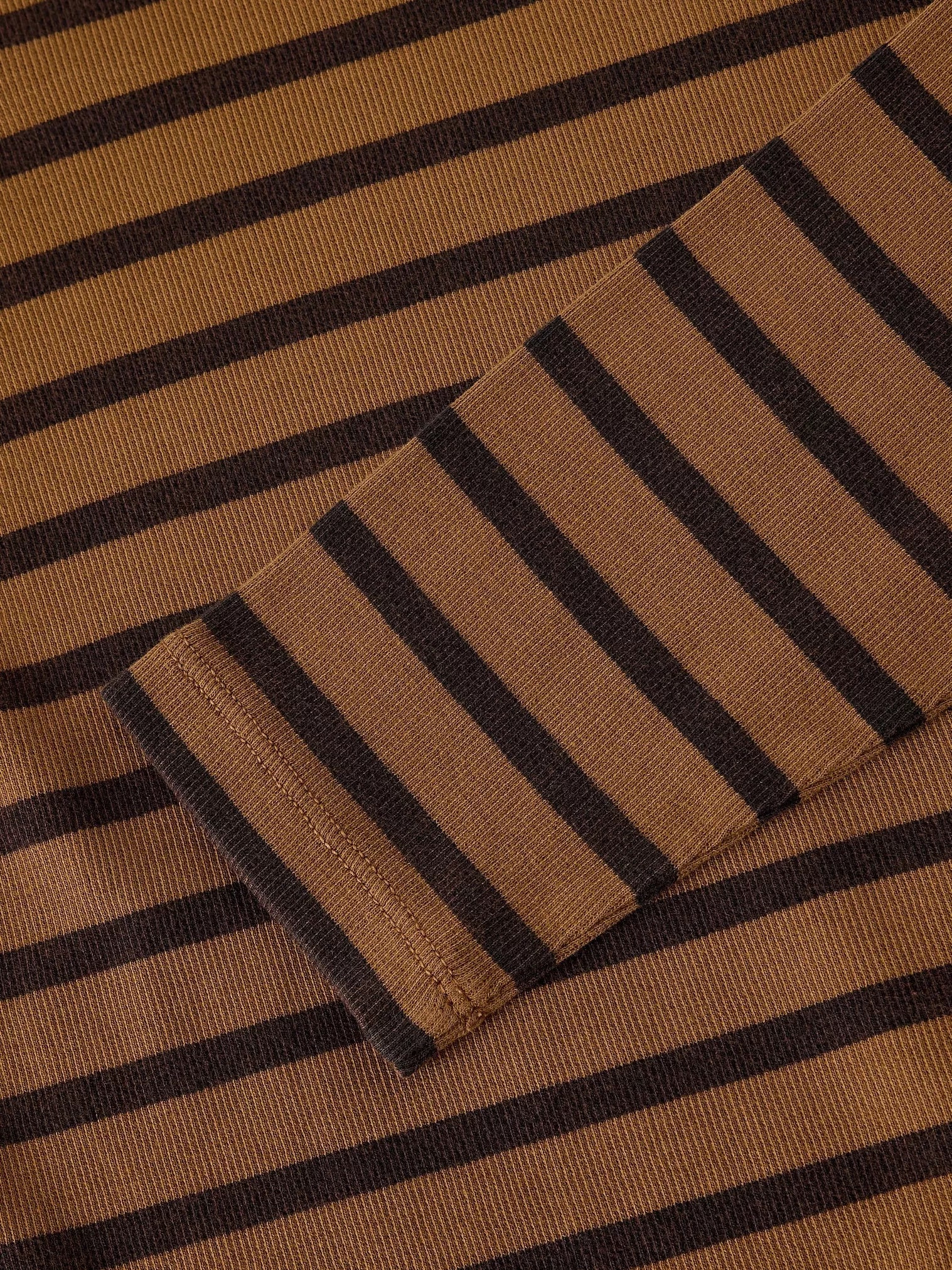 A close-up of a ribbed knit fabric with horizontal stripes in warm tan and dark brown, showing a folded cuff detail.