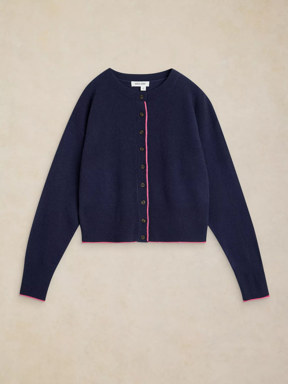 A navy blue cropped cardigan sweater with a pink piping accent along the button placket and cuffs, laid flat on a textured beige background.