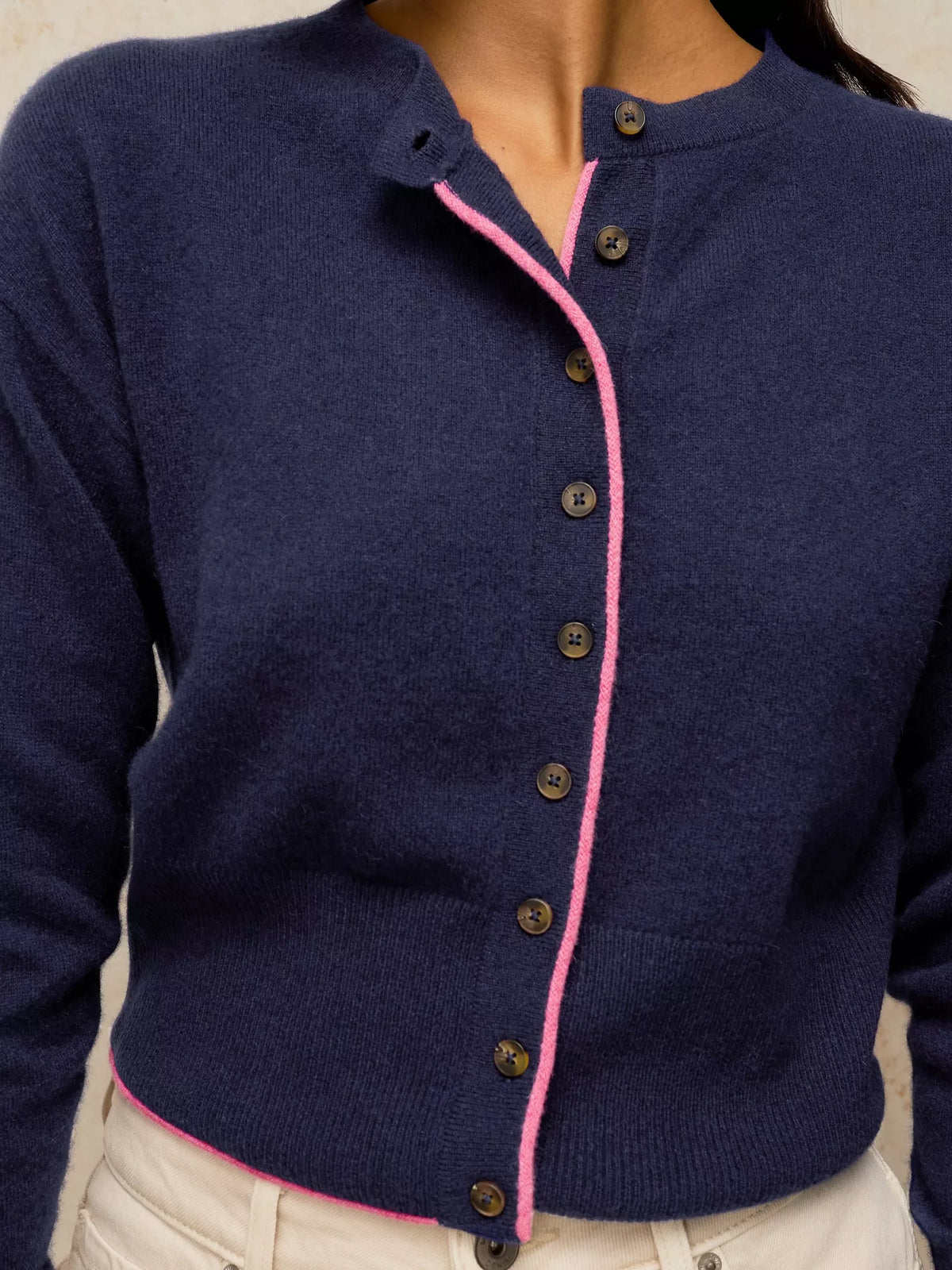 A close-up of a navy blue knit cardigan sweater with a contrasting pink trim along the button placket and hem, worn by a model.