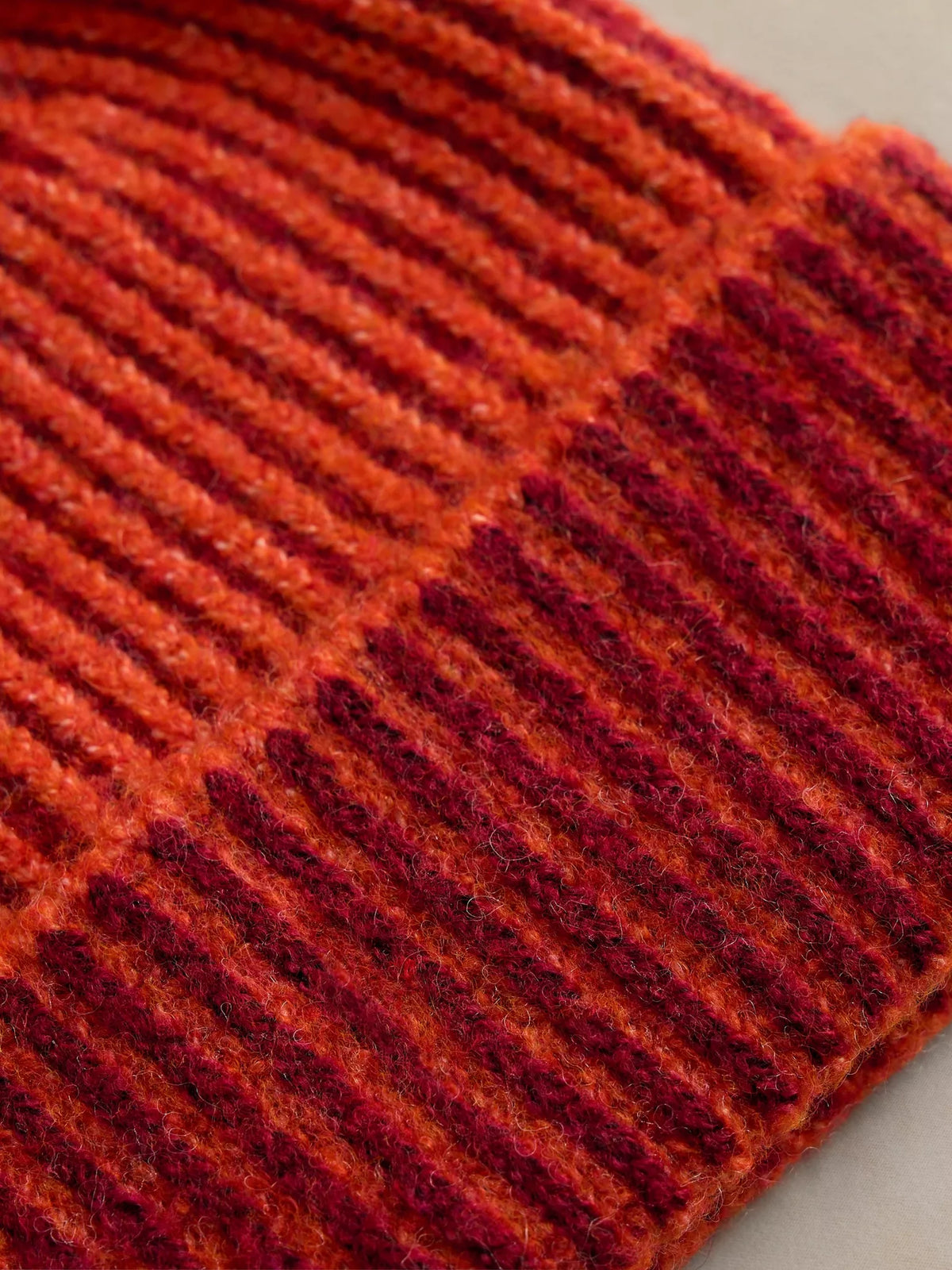 Close-up of a ribbed knit fabric in warm rust orange and deep burgundy red tones.