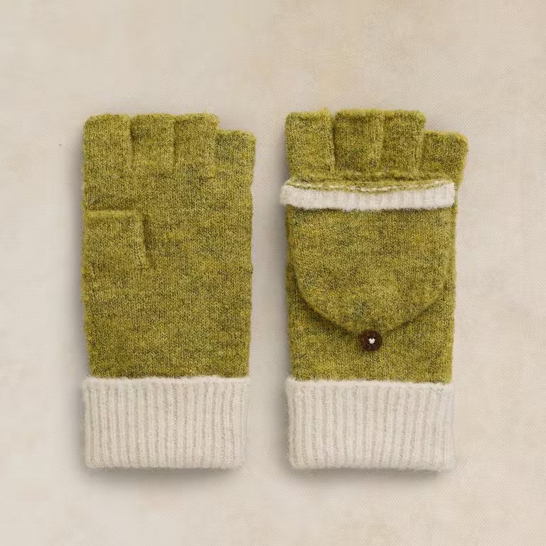 A pair of olive green and cream knit fingerless gloves with a small brown button detail, displayed flat on a textured beige background.