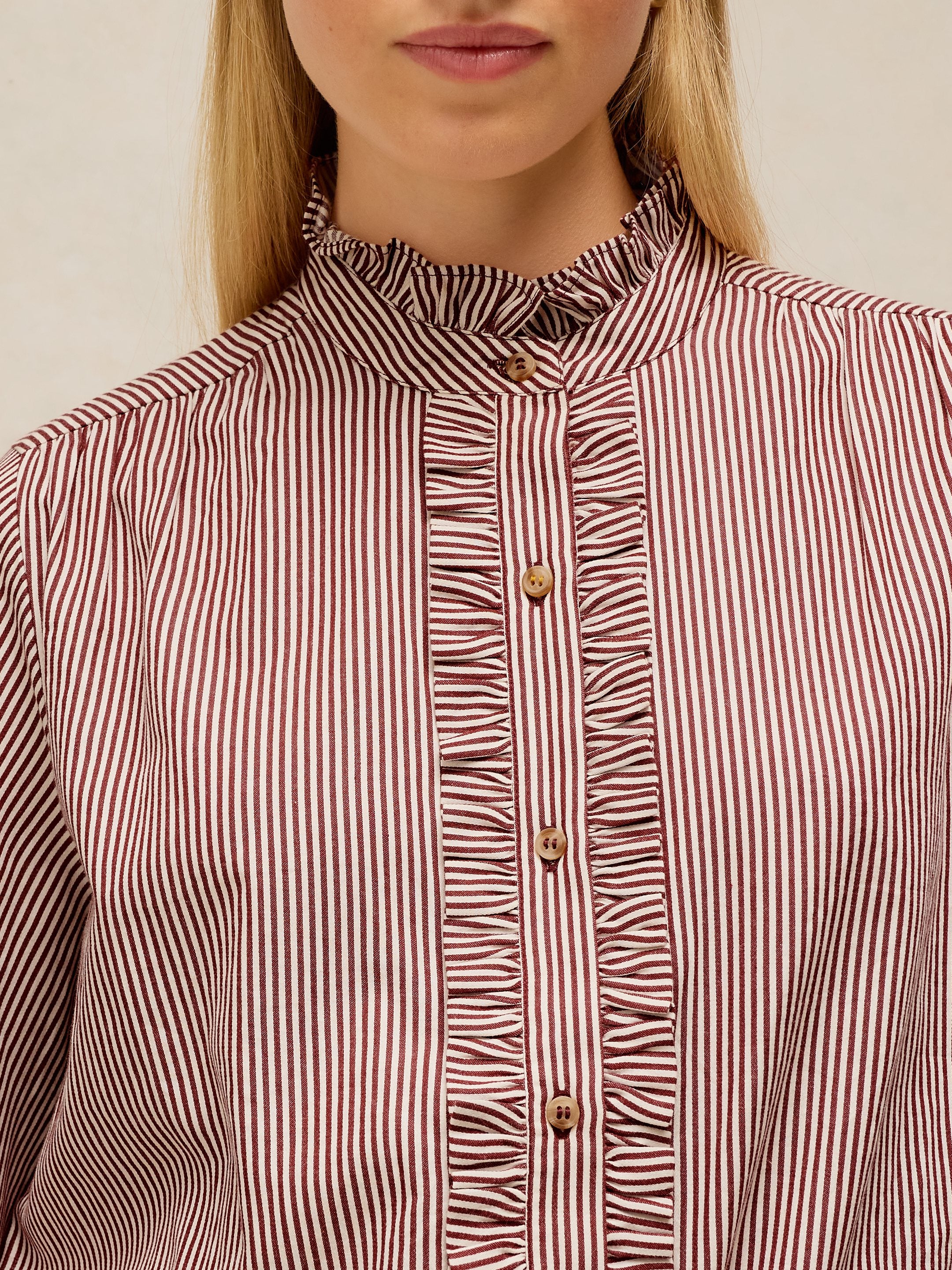 Close-up of a woman wearing a ruffled high-neck blouse with vertical red and white stripes and gold buttons.