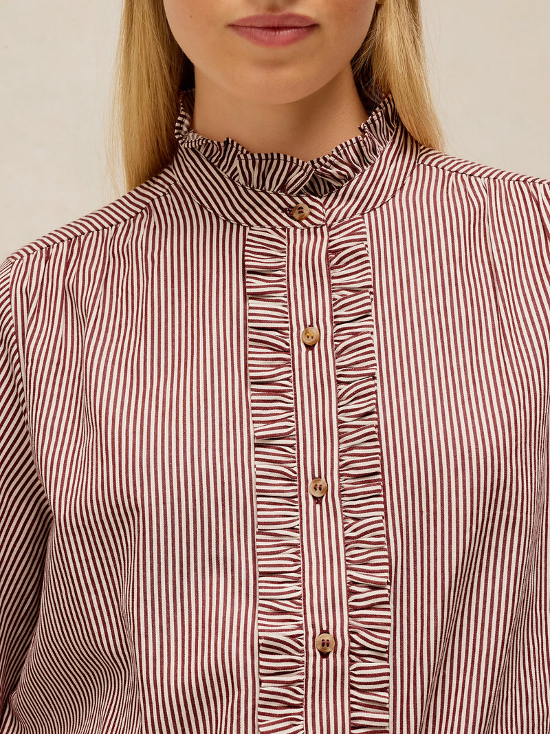 Close-up of a woman wearing a ruffled high-neck blouse with vertical red and white stripes and gold buttons.