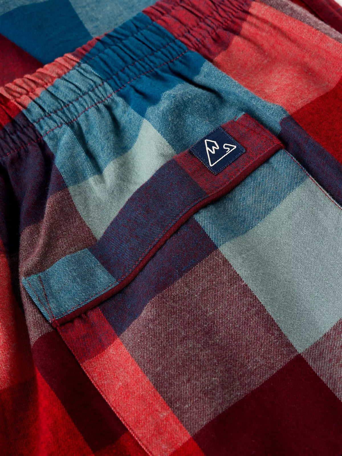 Close-up of a plaid garment, likely shorts or pants, featuring an elastic waistband and a front pocket with a small black brand tab. The fabric has a heathered texture in red, blue, and muted gray tones.