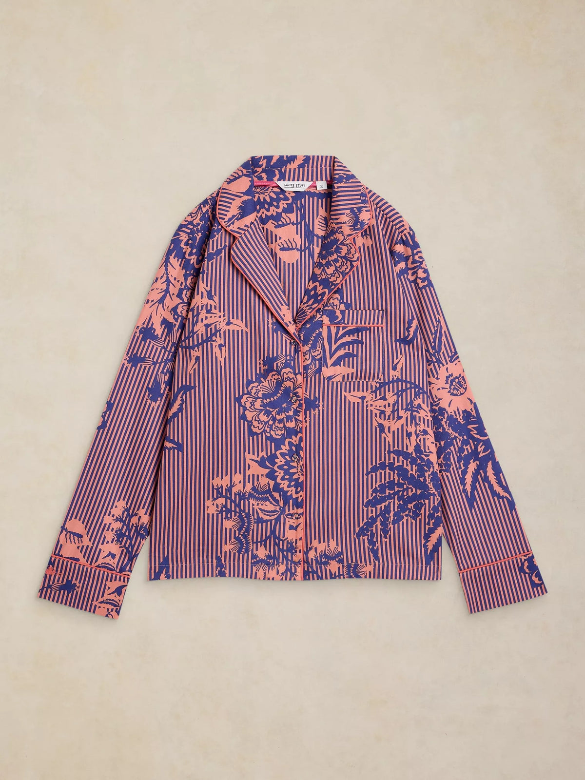 A long-sleeve button-up shirt with a patterned design featuring vertical navy and pink stripes overlaid with a pink floral and botanical print, laid flat on a textured beige background.