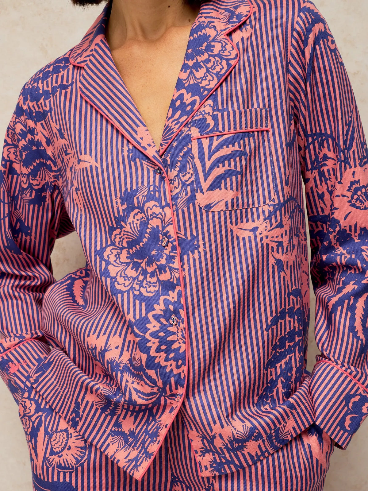 A close-up of a person wearing a long-sleeve pajama shirt with a pink and blue floral print over a blue and pink vertical stripe base.