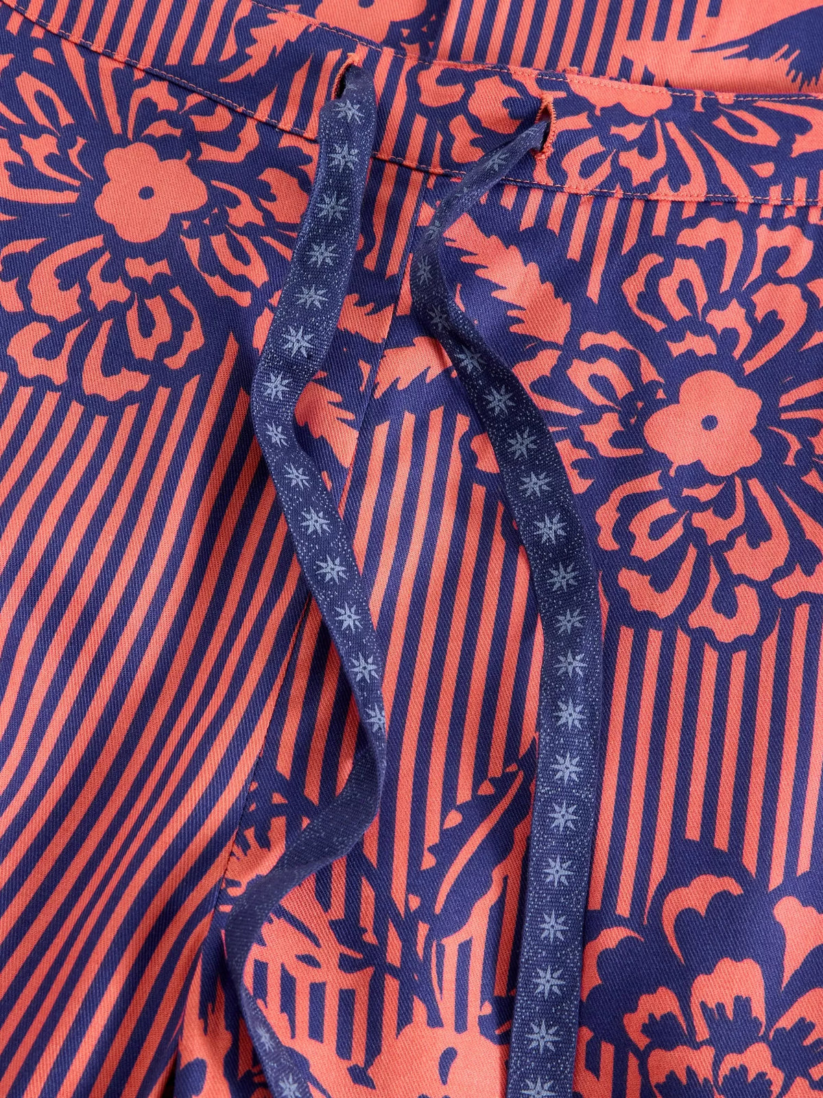 Close-up of a patterned garment featuring navy blue and coral orange floral and striped print, with a matching navy drawstring threaded through a pocket.