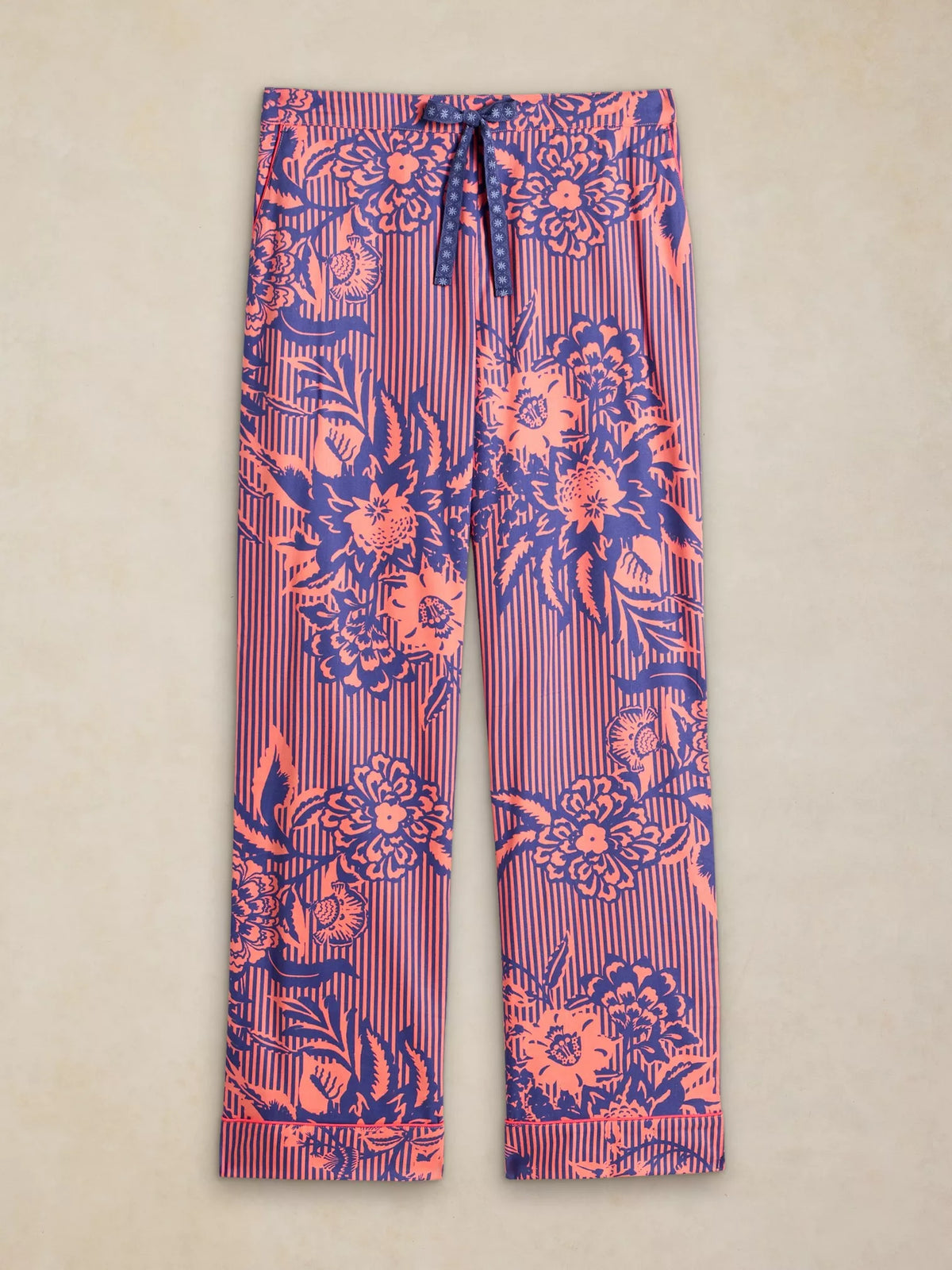 A pair of women's wide-leg lounge pants featuring a vibrant floral and stripe pattern in pink, purple, and red, laid flat against a neutral beige background.