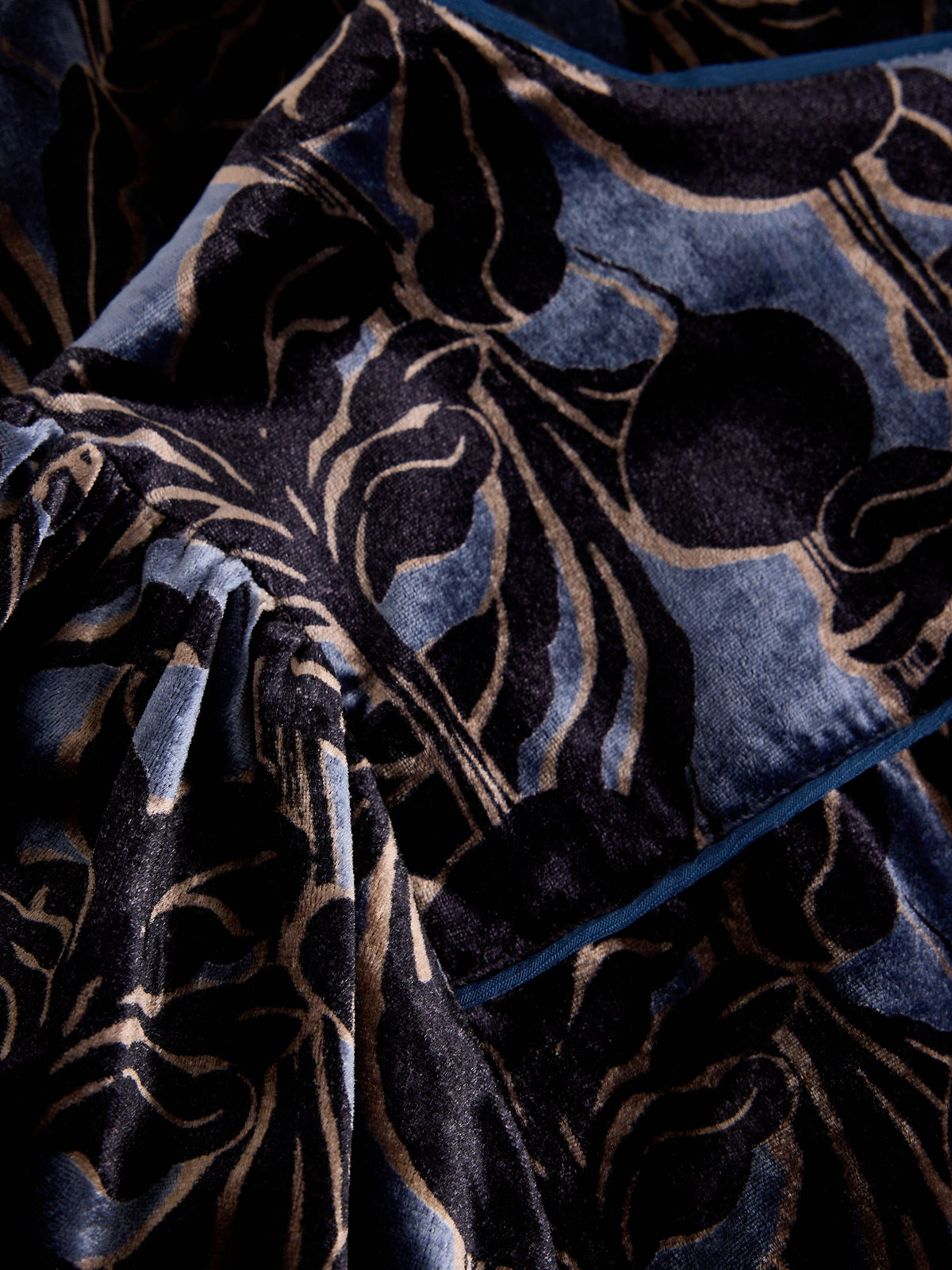 A close-up of a luxurious velvet fabric with a dark navy blue base and an ornate, raised beige floral pattern.