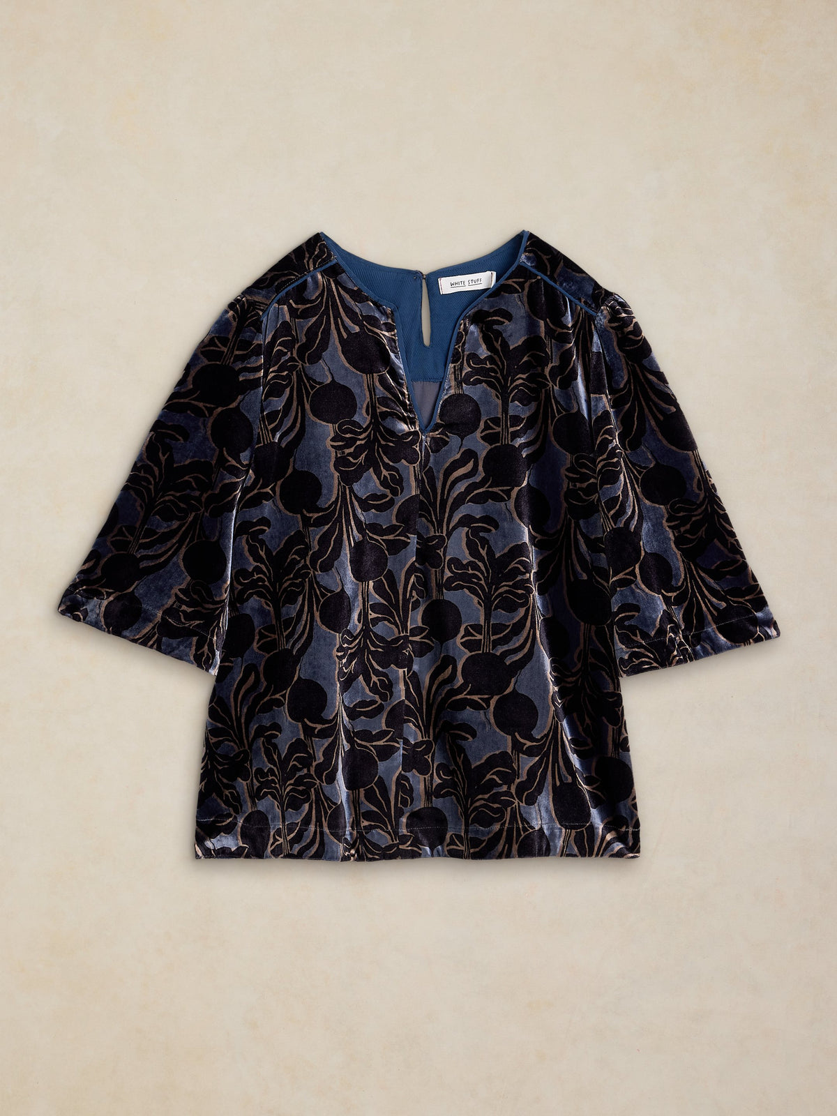 A short-sleeve velvet top with a dark floral pattern, laid flat on a textured beige background.