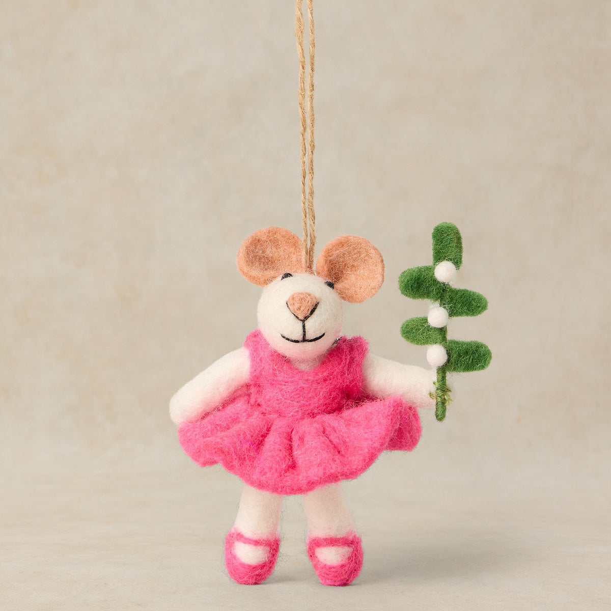 A handmade felt mouse ornament dressed in a pink tutu and ballet shoes, holding a small green sprig, hanging from a natural jute string against a neutral beige background.