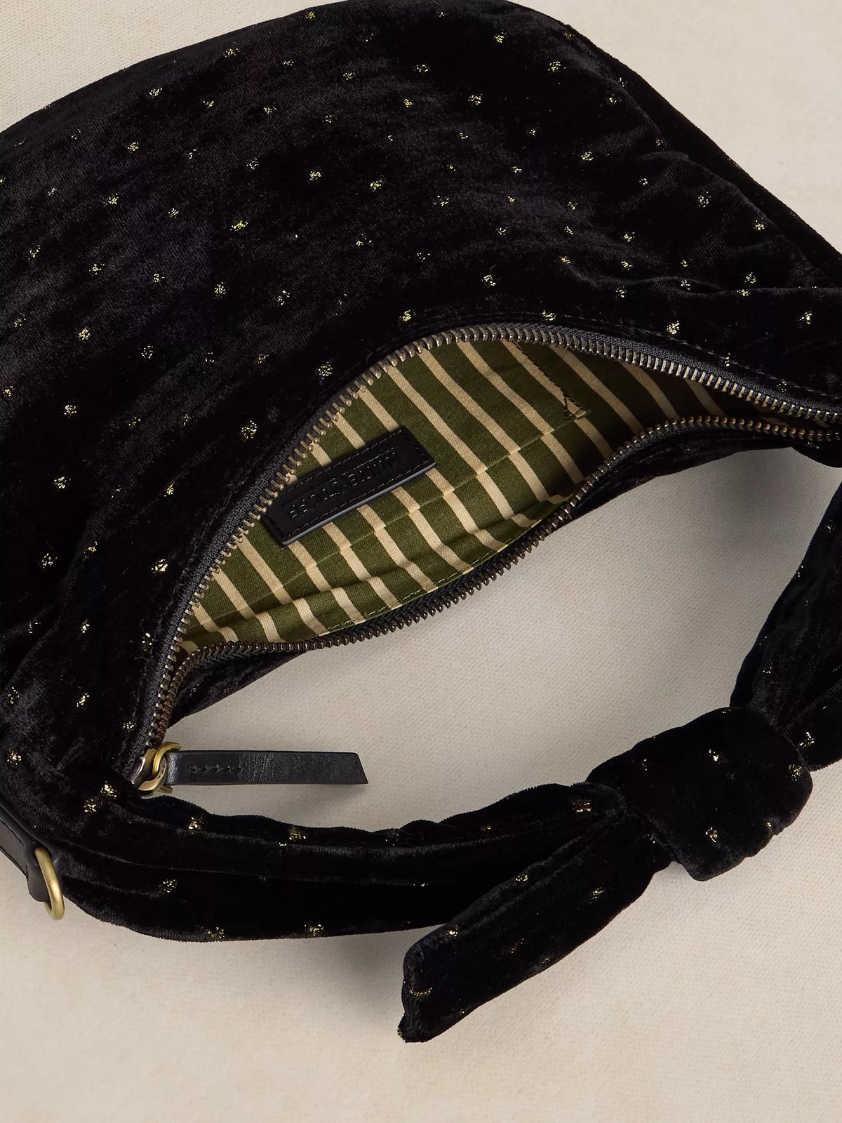 Close-up of a black velvet shoulder bag with small gold star details, shown open to reveal a green and beige striped interior lining.
