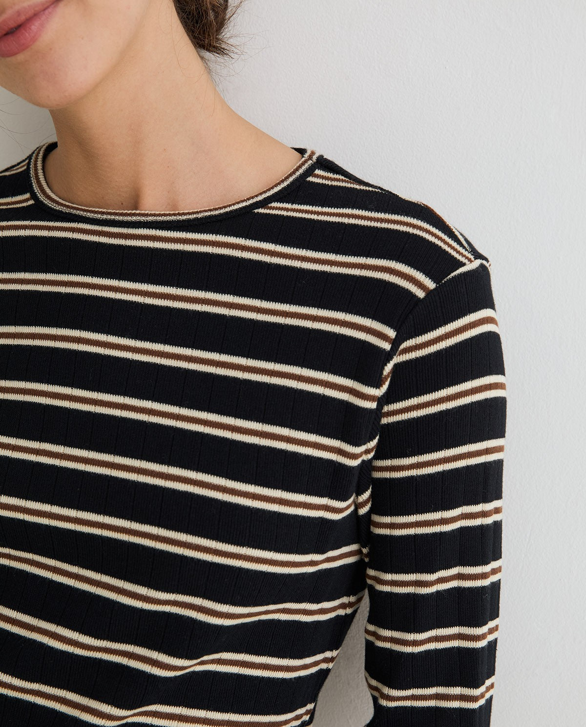 Close-up of a person wearing a ribbed long-sleeve top with horizontal stripes in black, cream, and brown against a plain light background.