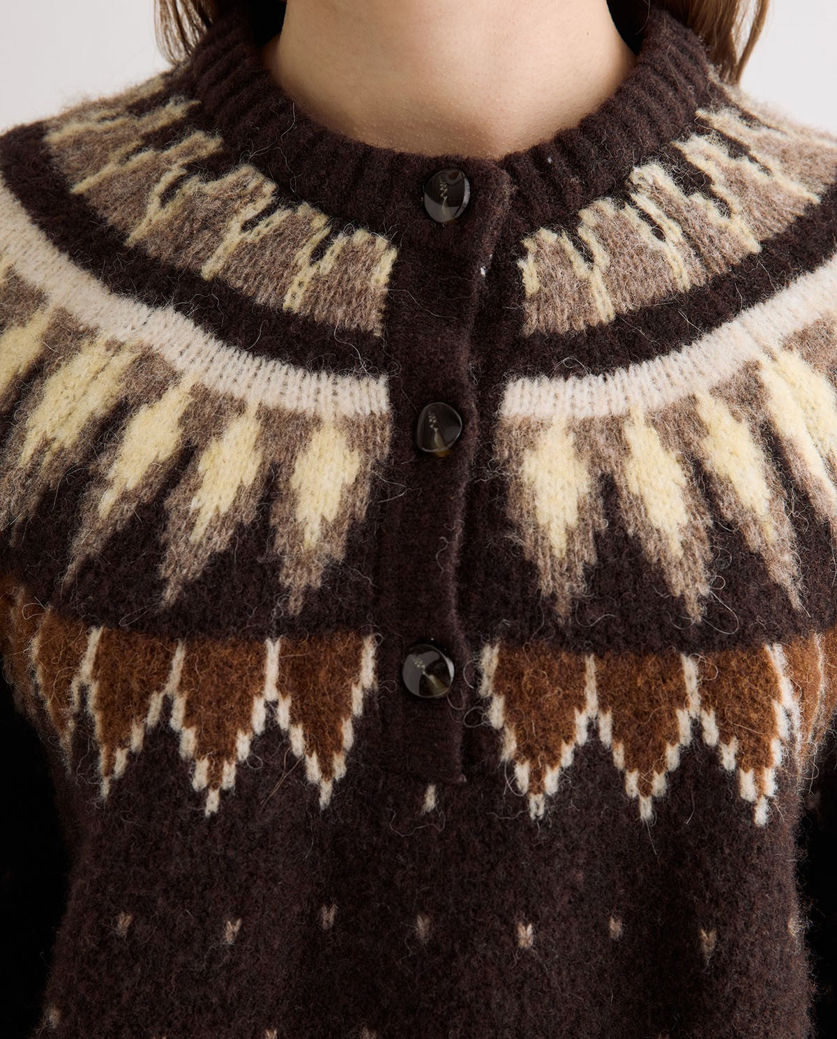 Close-up of a person wearing a fuzzy knit cardigan sweater with a brown, cream, and tan Fair Isle pattern and dark buttons.