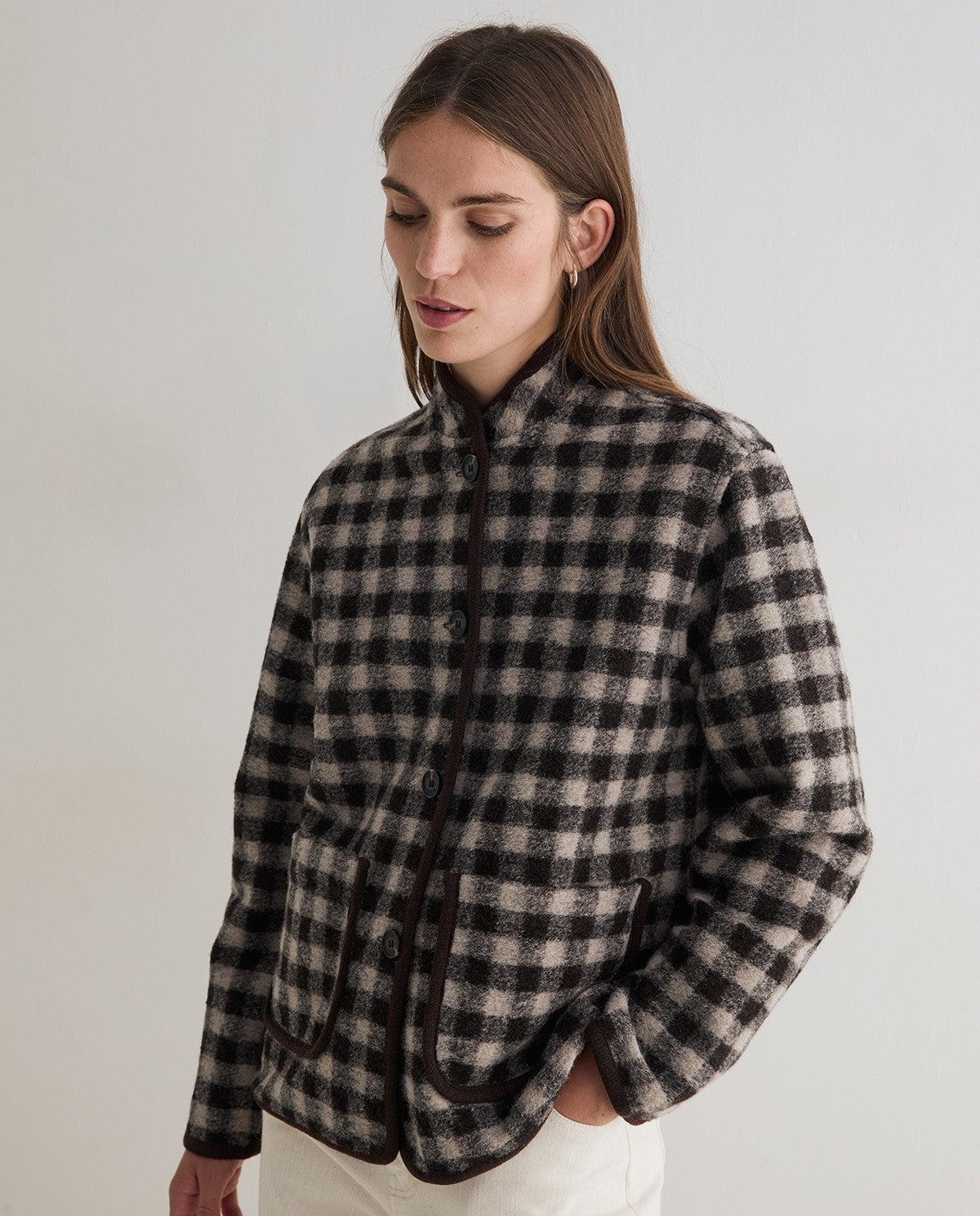 A woman wearing a black and beige checkered wool-blend jacket with dark brown trim, photographed against a plain light gray studio background.