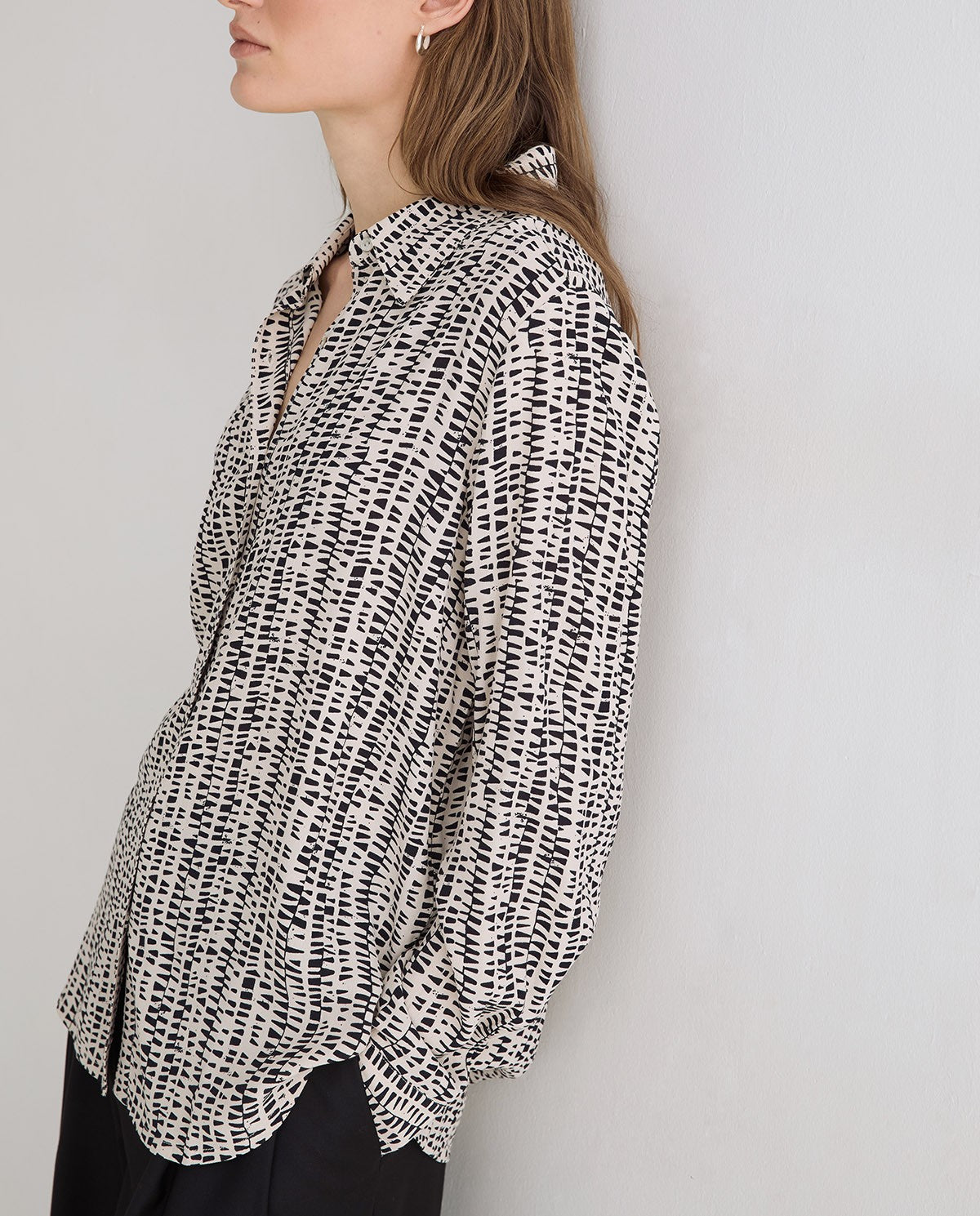 A woman wearing a black and white abstract patterned button-up shirt, shown in a side profile against a plain light gray wall.