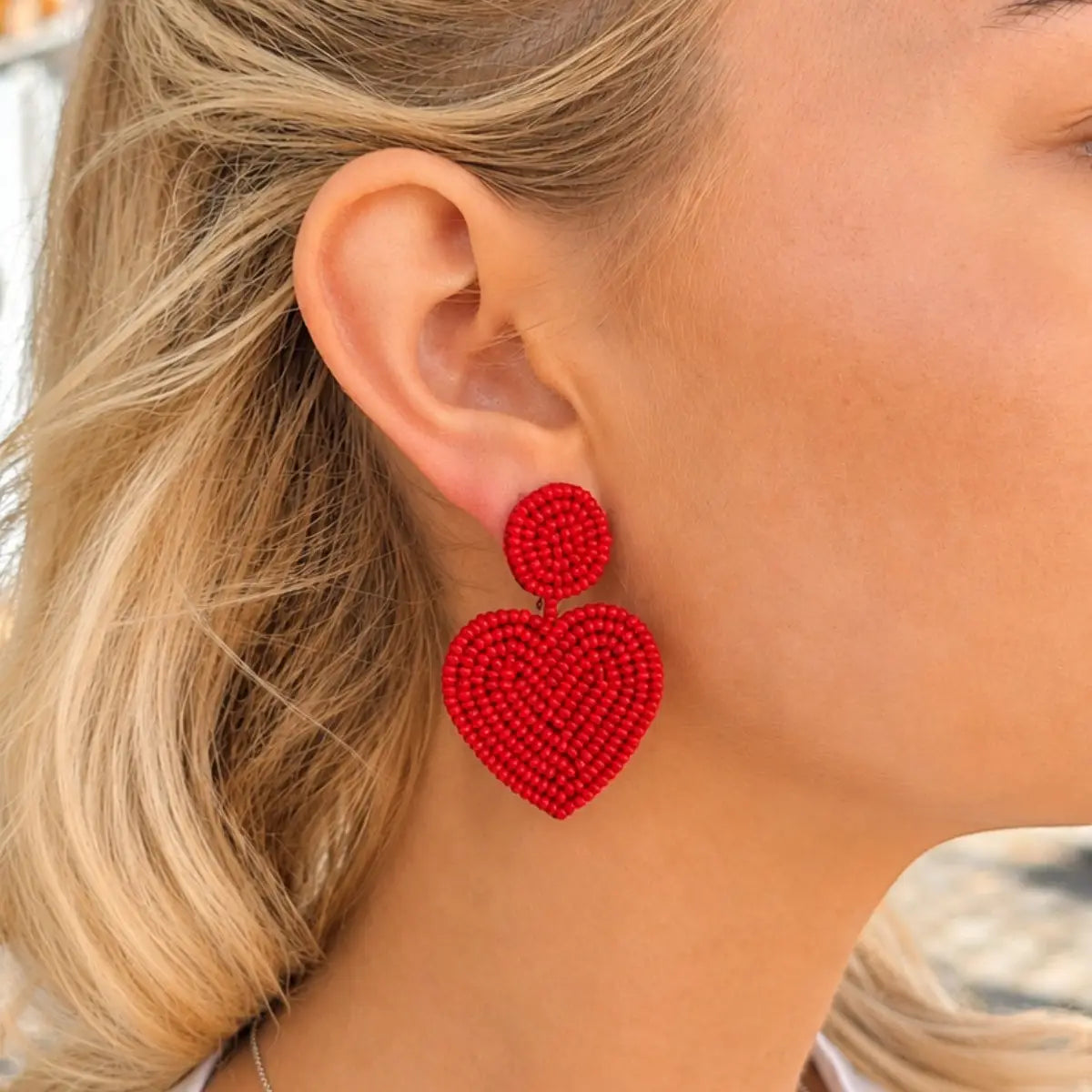 Close-up of a person wearing red heart-shaped earrings with blurred background