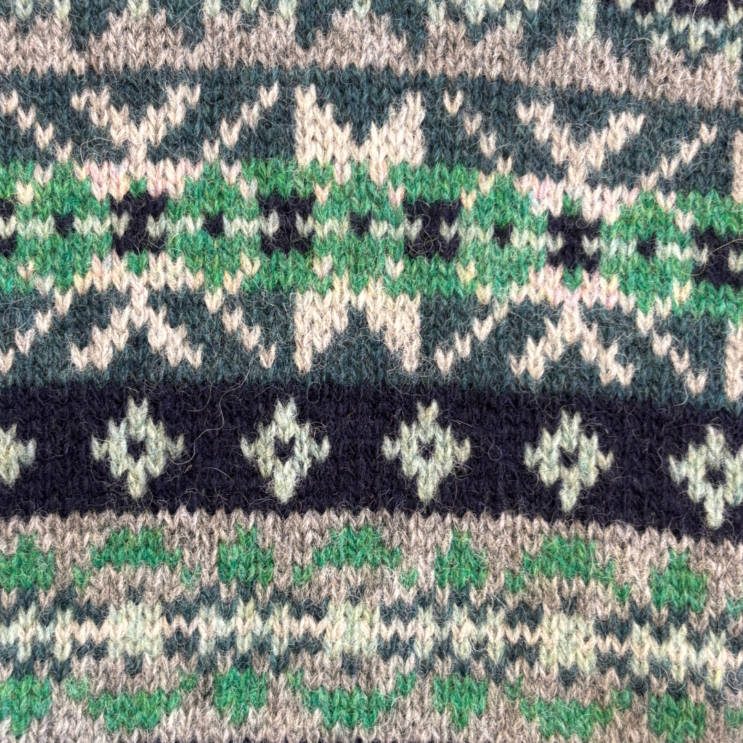 Close-up of hand-knitted fabric with a Fair Isle pattern in green, beige, and black.