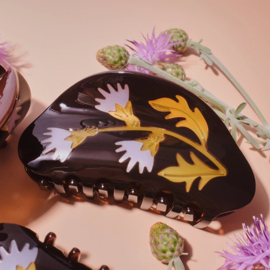 Decorative hair clip with floral design on a pink background with flowers.