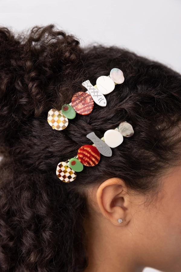 Close-up of a person's hair with colorful food themed hair clips on a neutral background