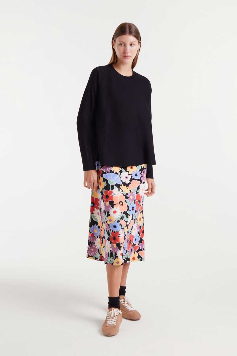 Woman wearing a black top and colorful floral skirt on a white background